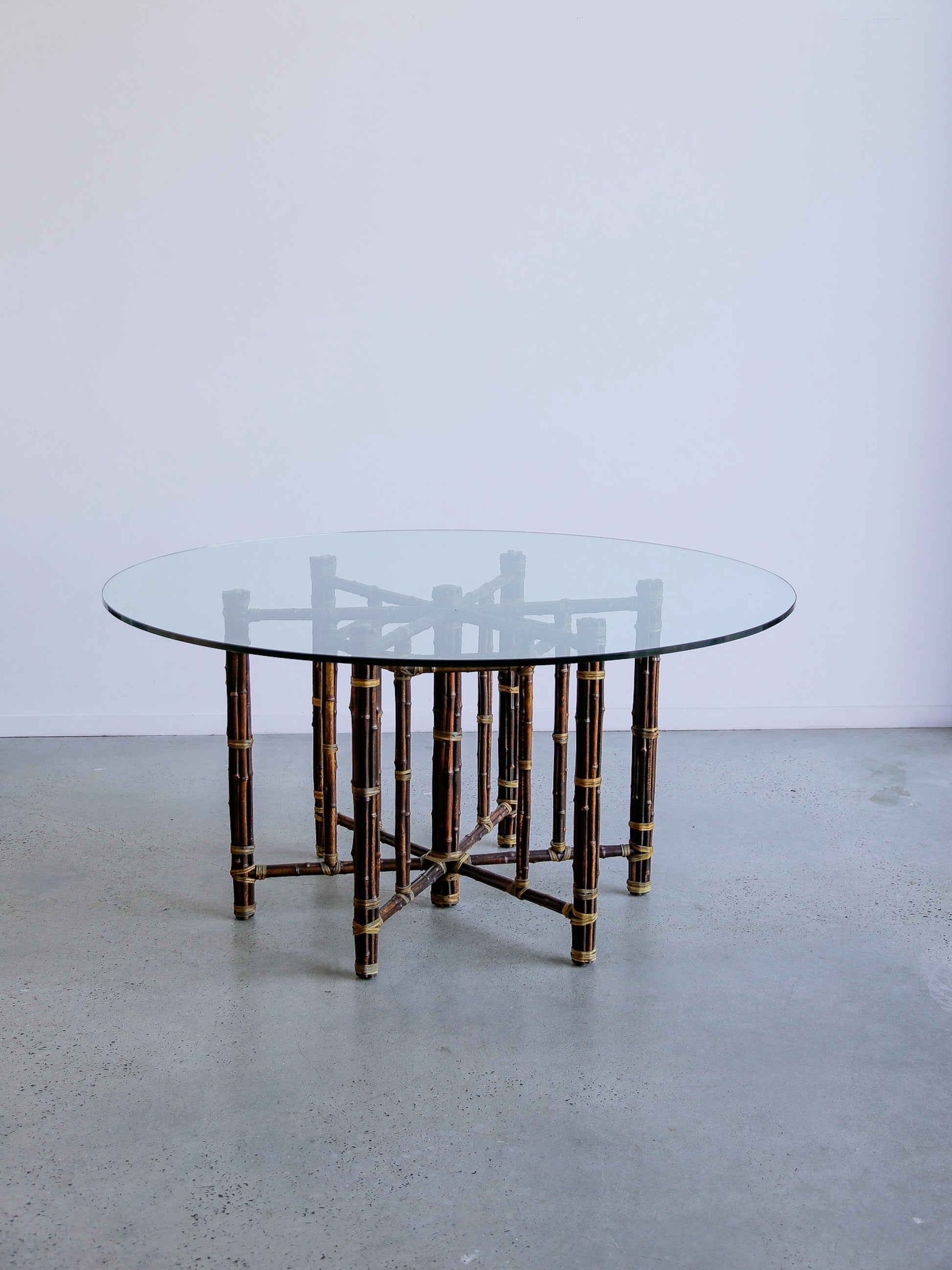 Round glass table with bamboo-style frame on a plain floor and wall background