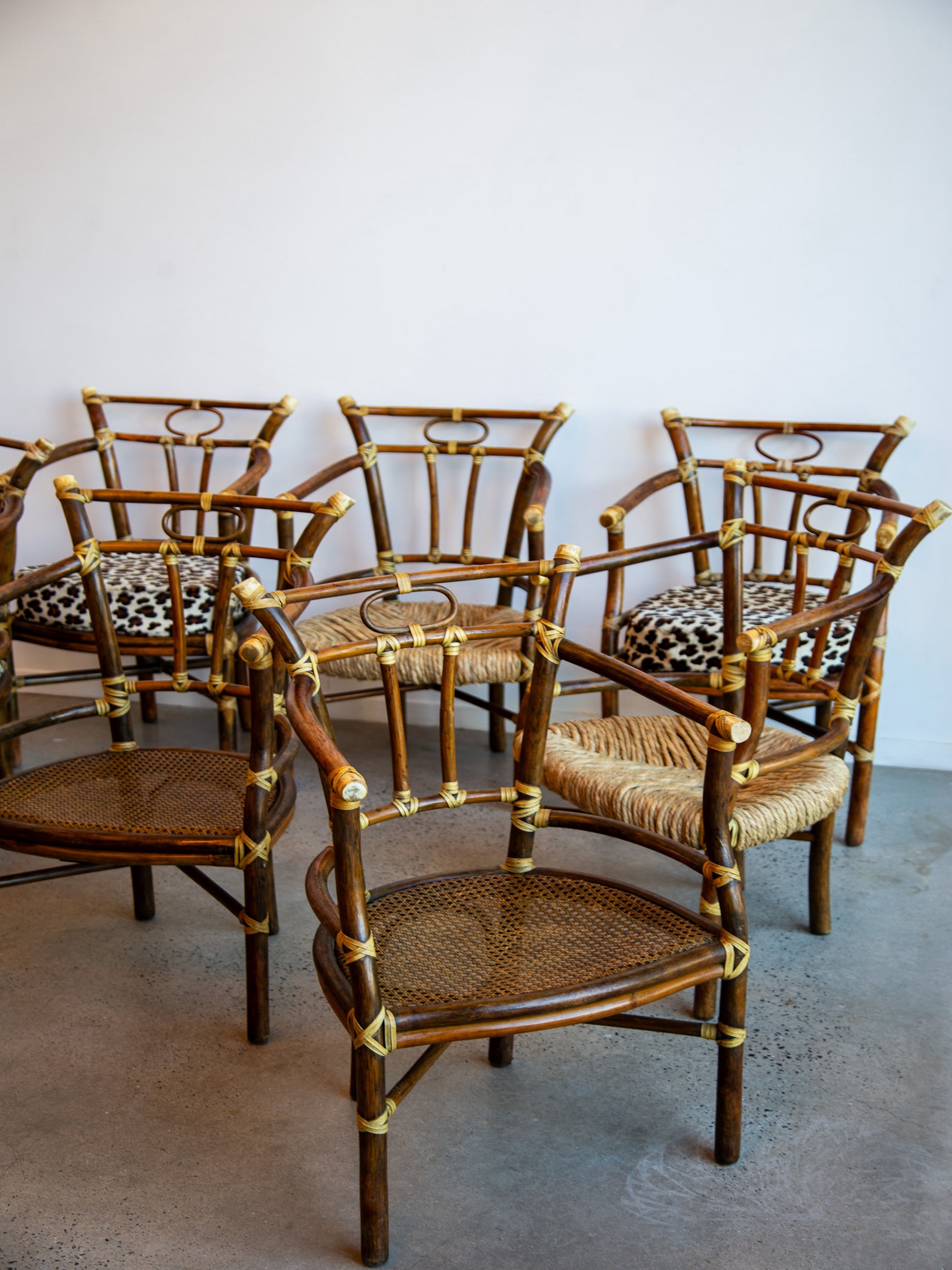 Set of bamboo chairs with woven seats and leopard print cushions on a concrete floor.
