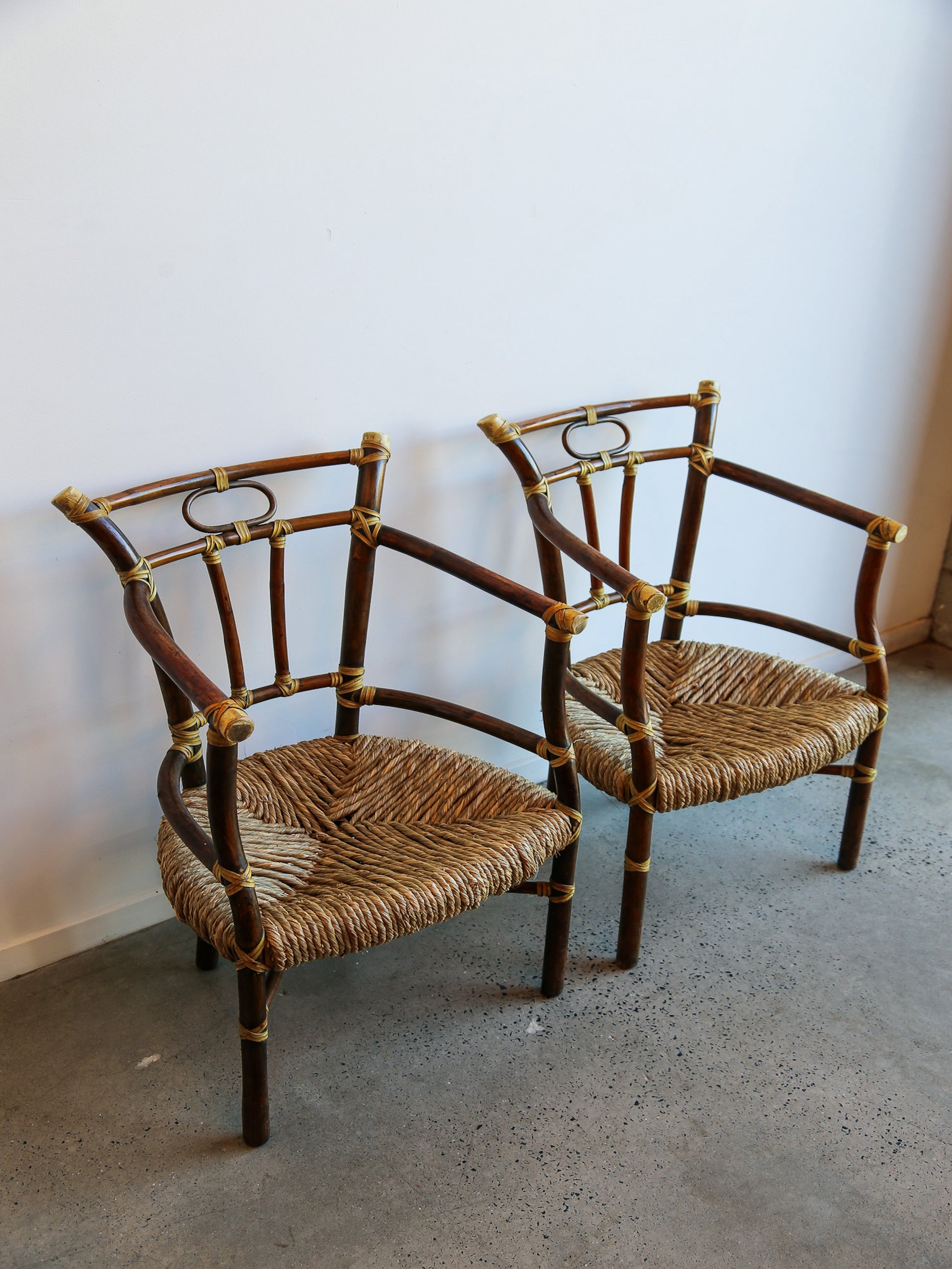 Two wicker chairs with bamboo frames on a concrete floor against a white wall.