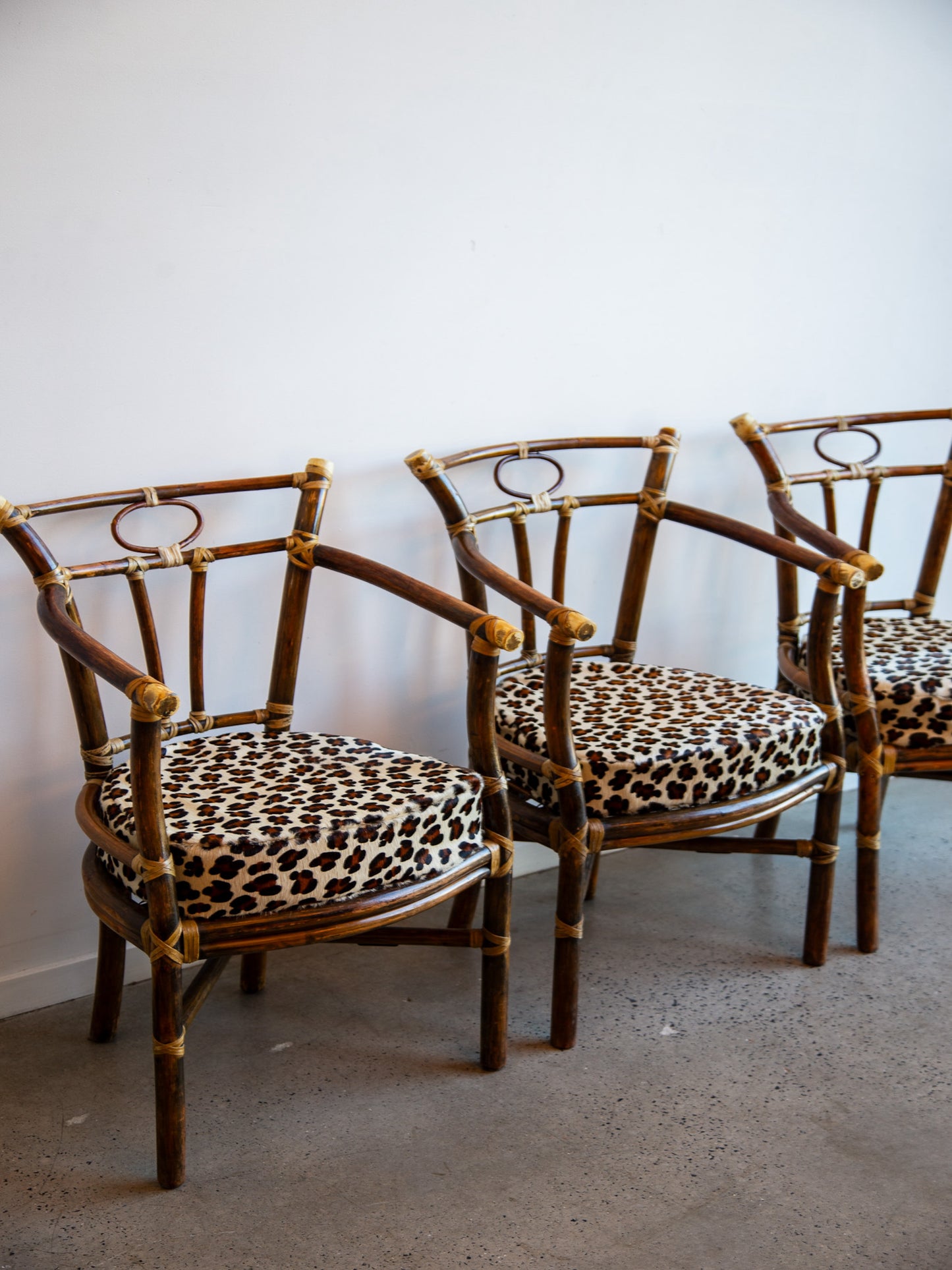 Three rattan chairs with leopard print cushions against a white wall.