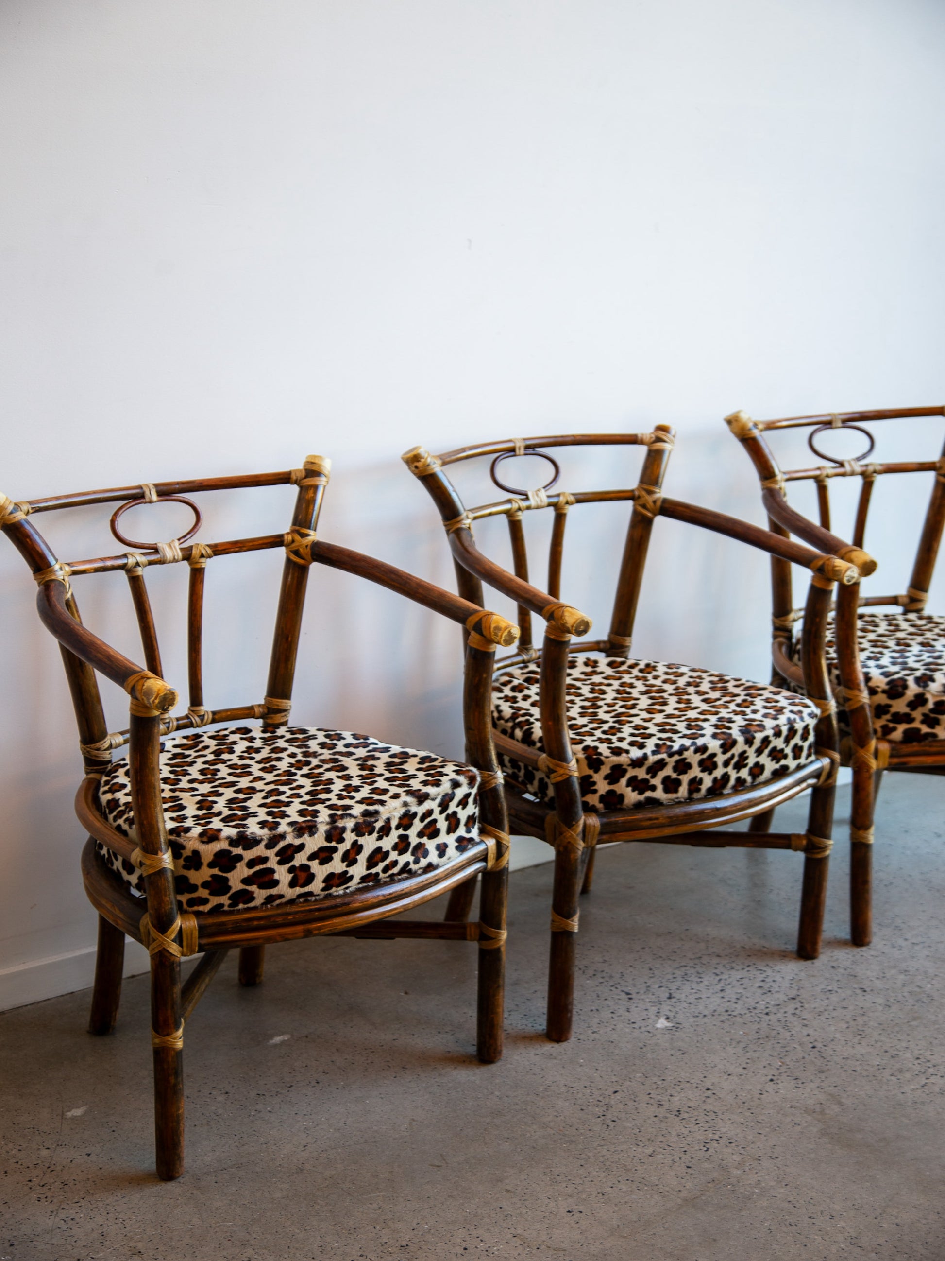 Three rattan chairs with leopard print cushions against a white wall.