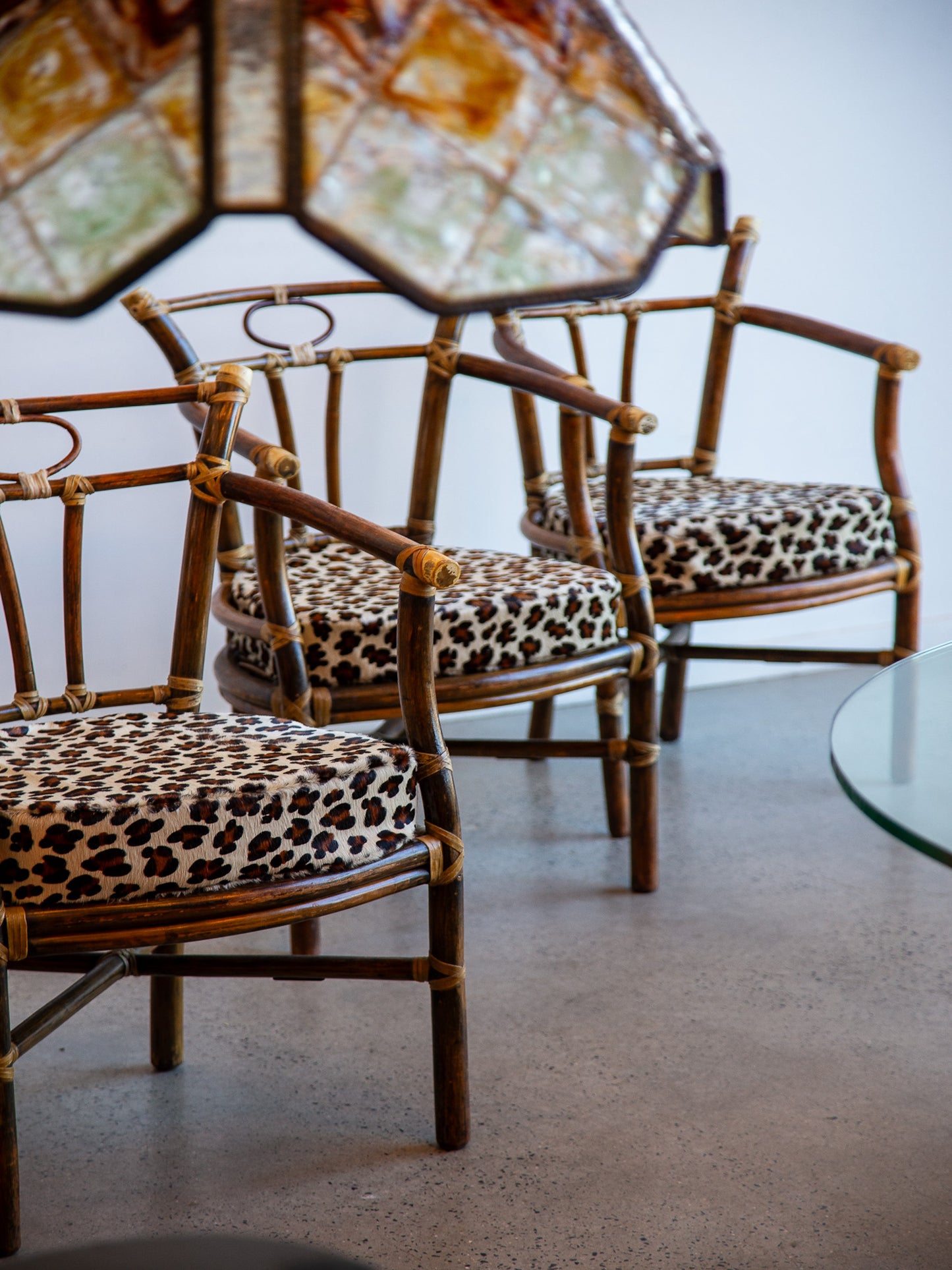 Rattan chairs with leopard print cushions in a room with a glass table.