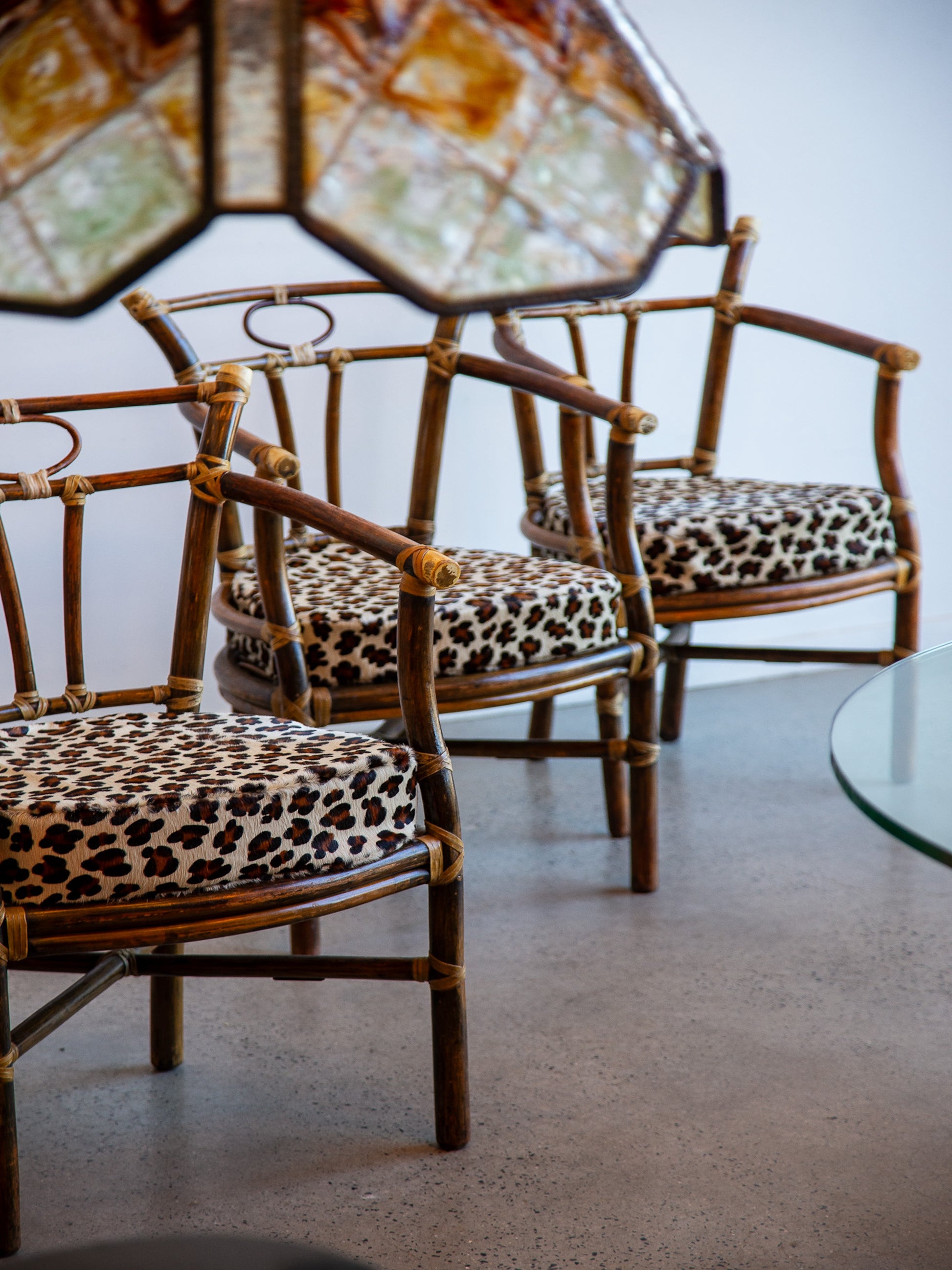 Rattan chairs with leopard print cushions in a room with a glass table.