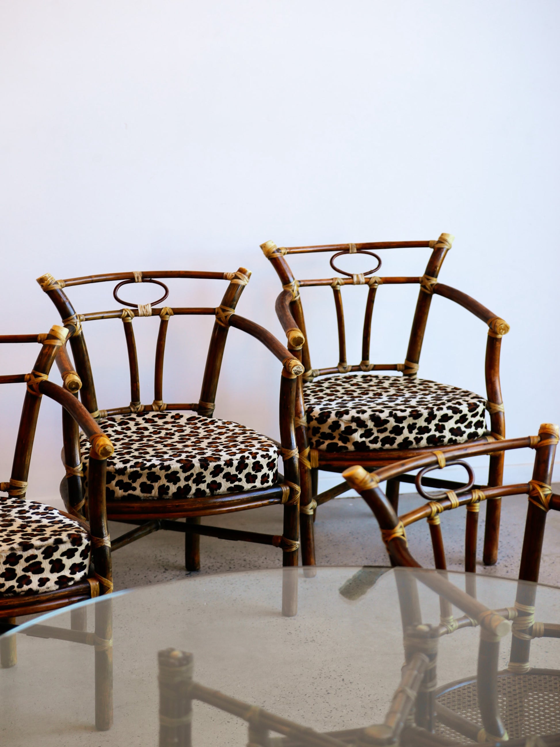 Three rattan chairs with leopard print cushions around a glass table on a light blue background