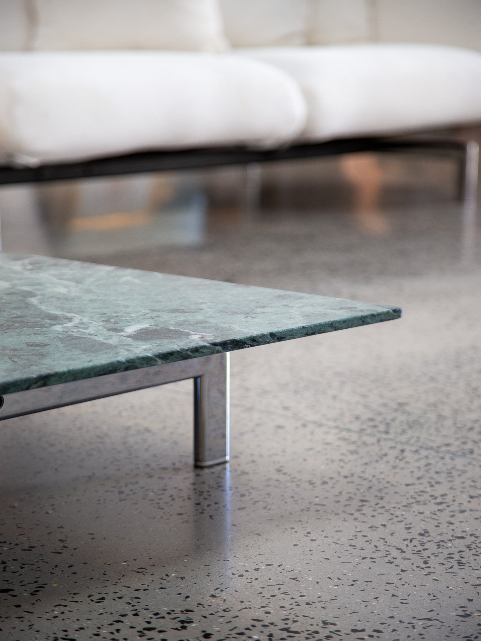 Green marble coffee table on a speckled concrete floor with a blurred white sofa in the background.