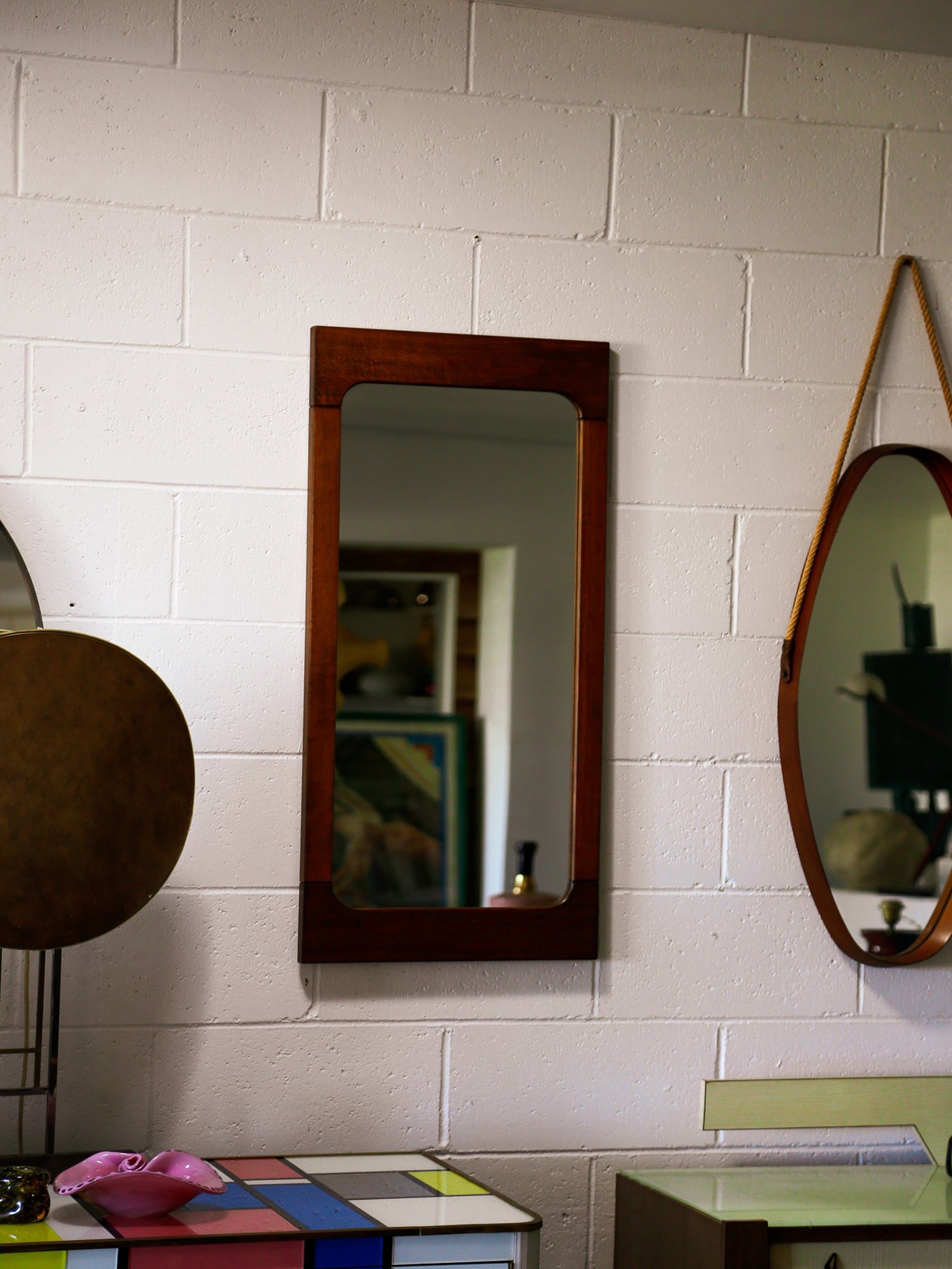 Three mirrors of different shapes and sizes on a white tiled wall.