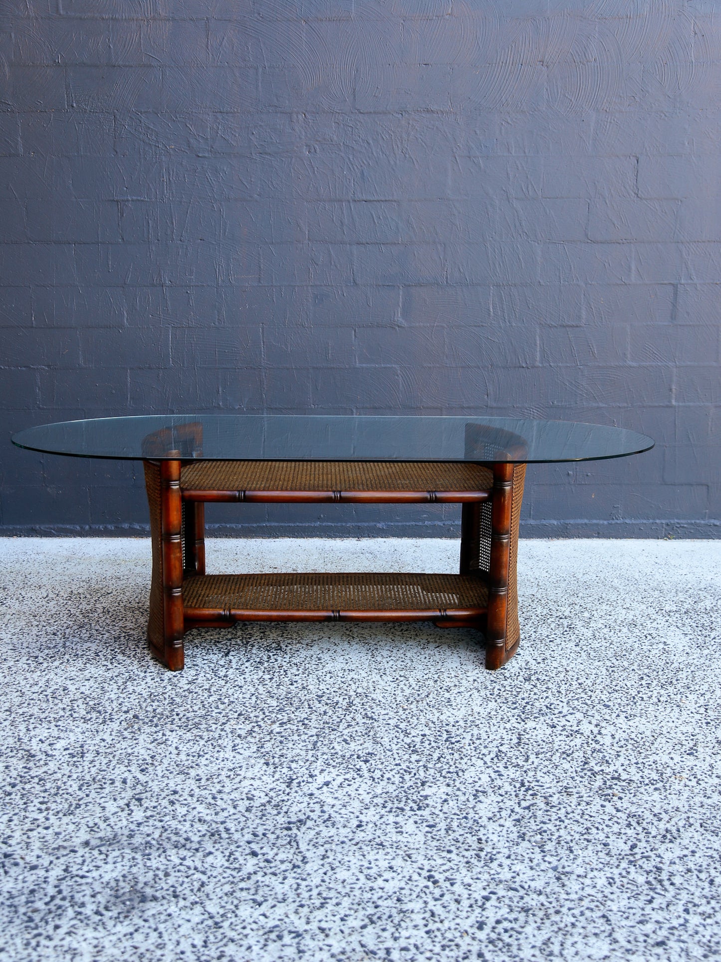 Glass-top coffee table with wooden base against a gray wall.