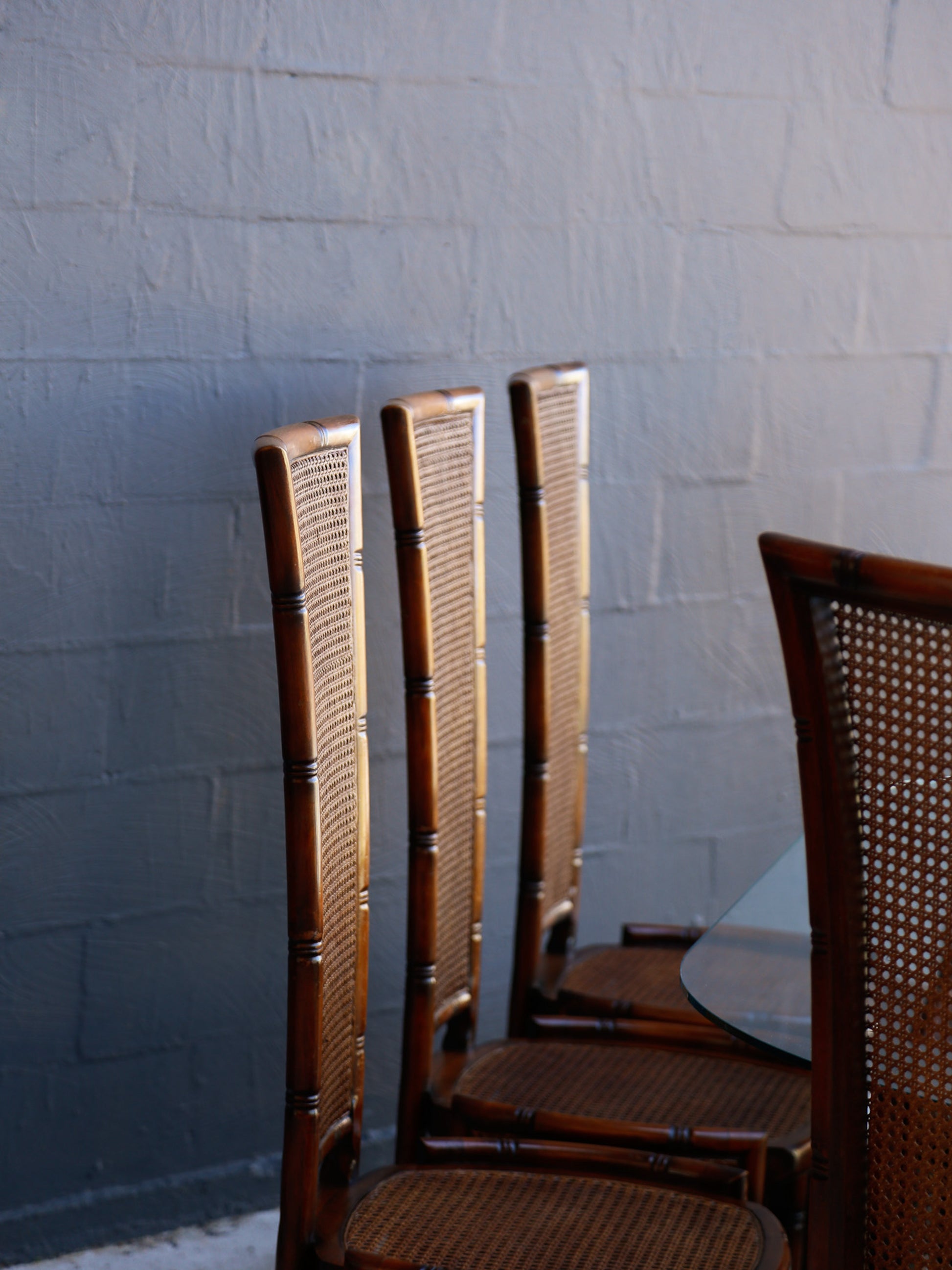 Four wooden chairs with woven backrests against a textured white wall.
