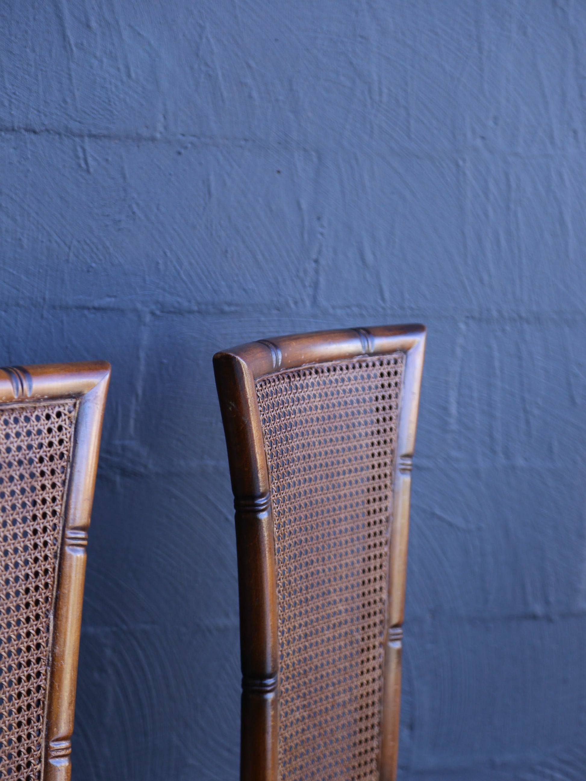 Two wooden chairs with wicker backrests against a textured blue wall.