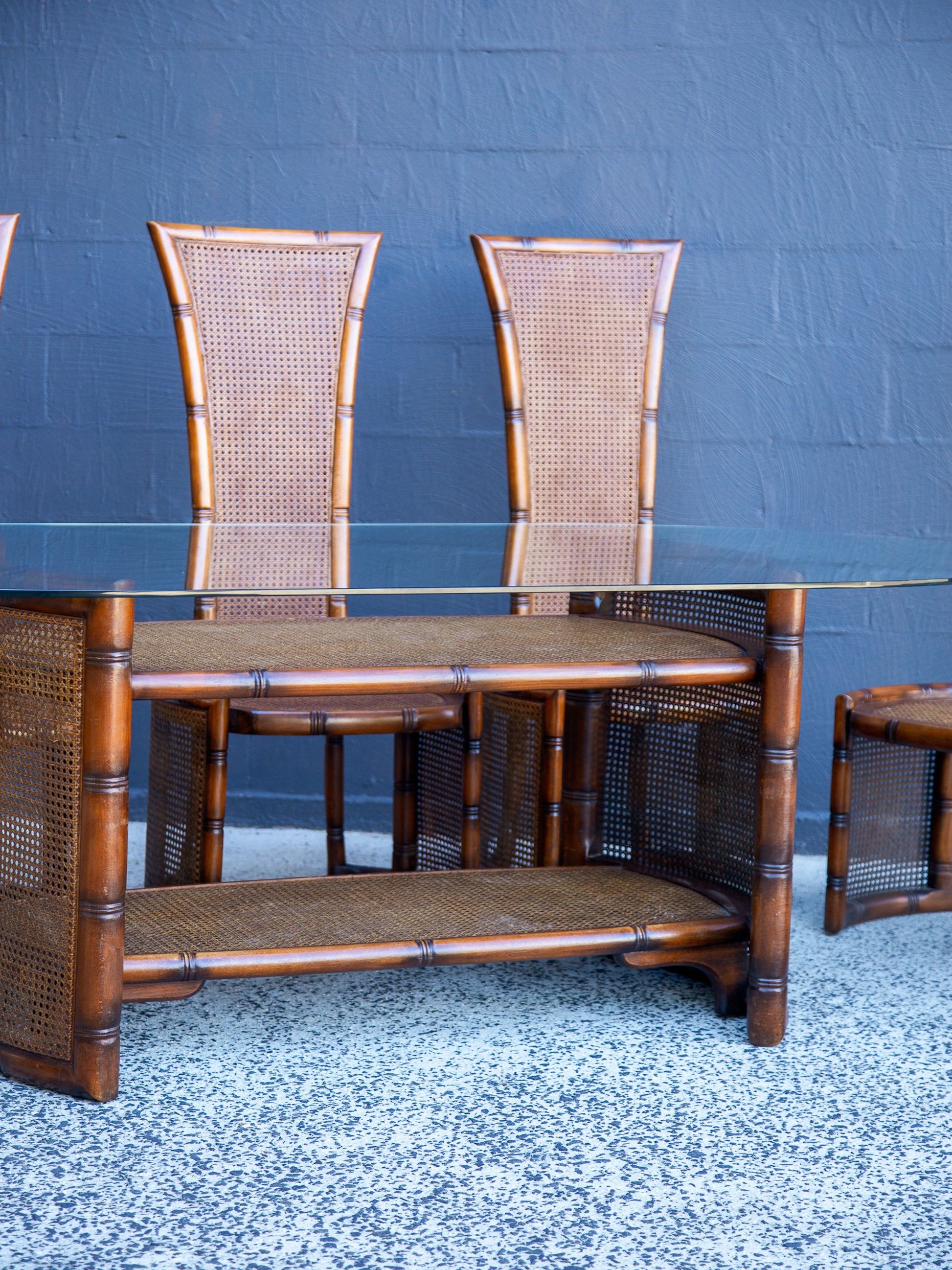 Rattan dining set with table and chairs against a blue wall.