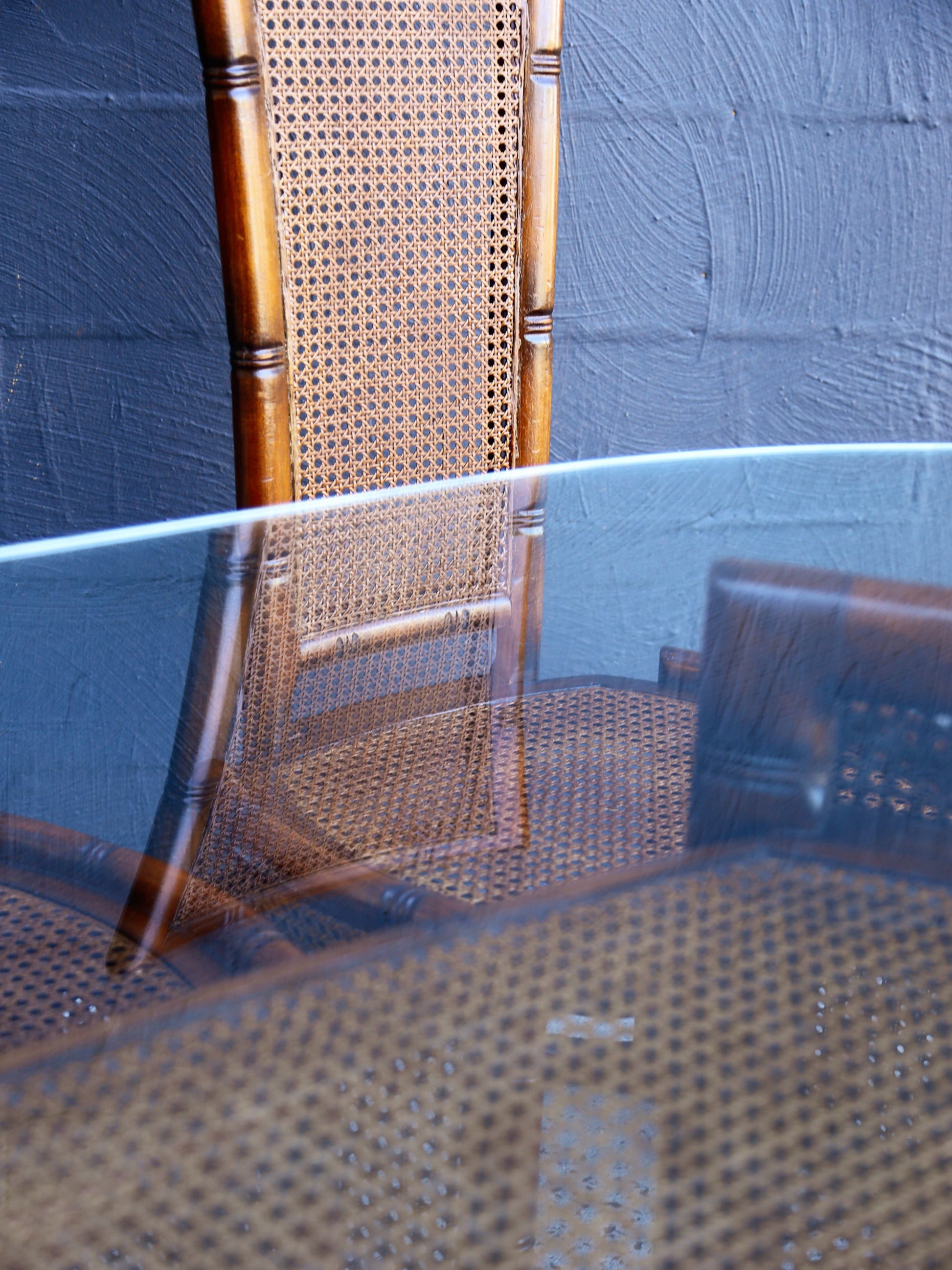 Wooden chair with wicker backrest reflected in a glass surface against a textured blue wall.