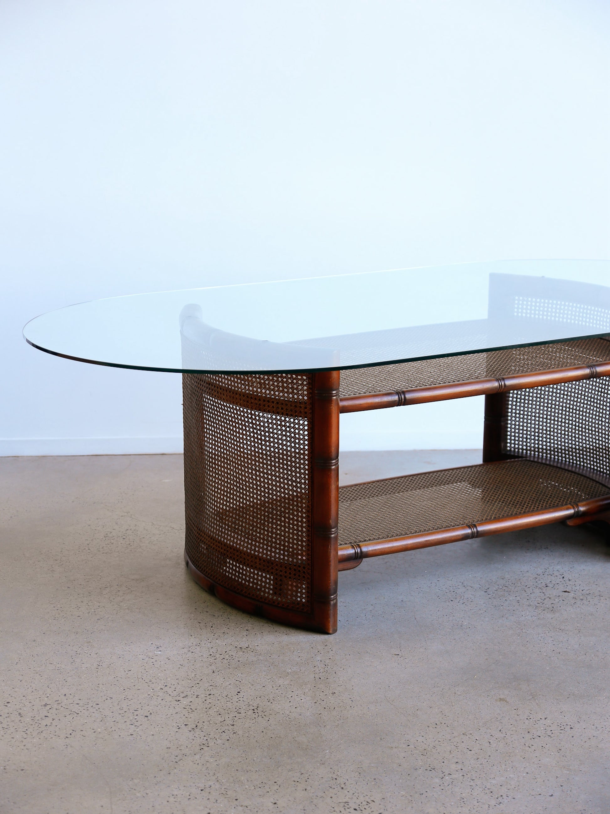 Glass-top coffee table with wicker base on a concrete floor