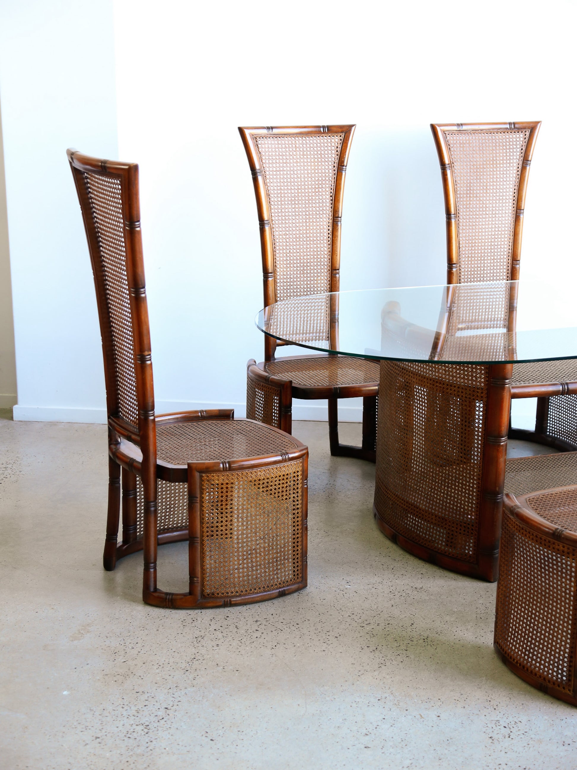 Wooden dining set with wicker chairs and a glass table on a light-colored floor.