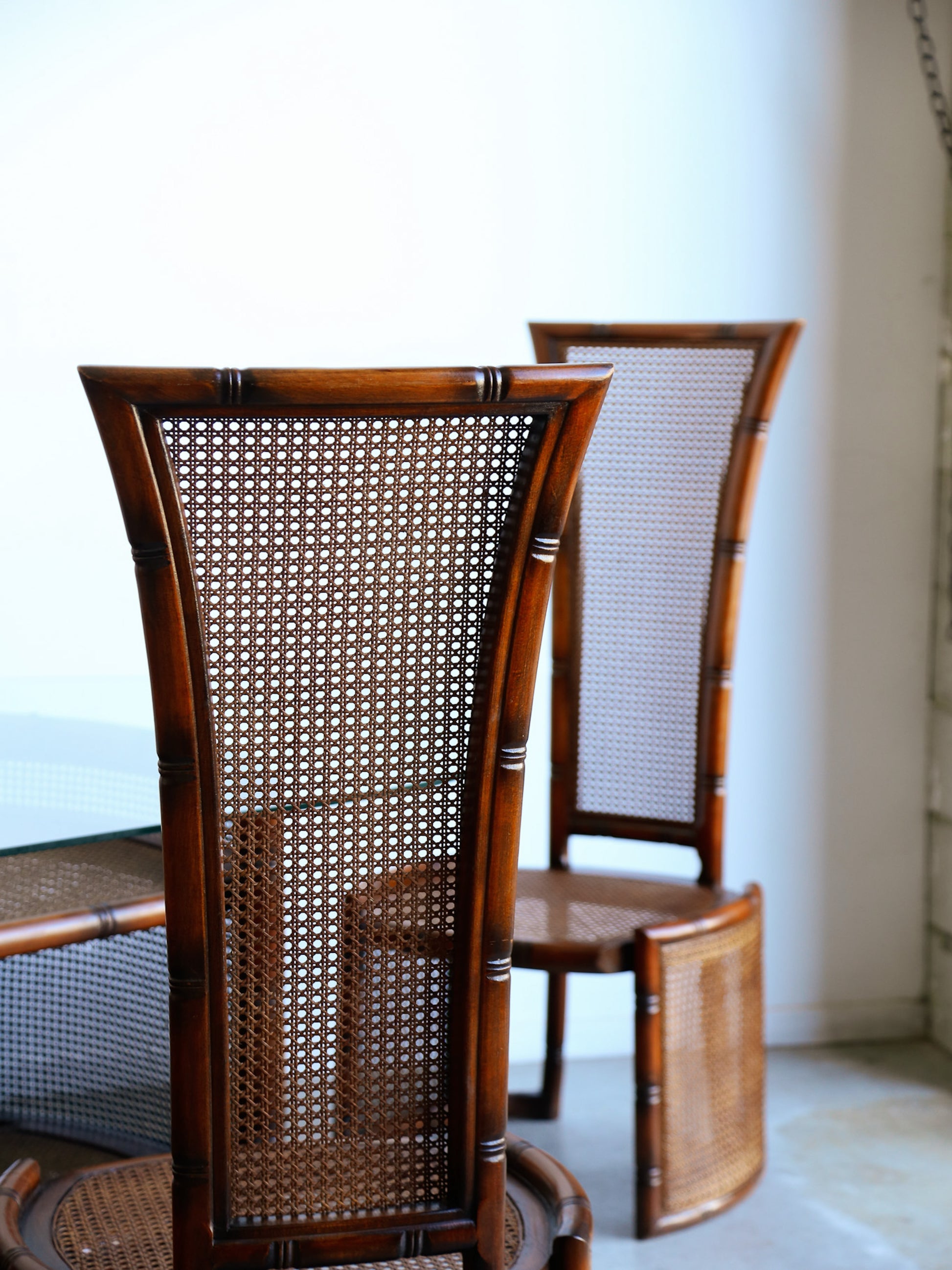 Two wooden chairs with wicker backrests in a room with a white wall.