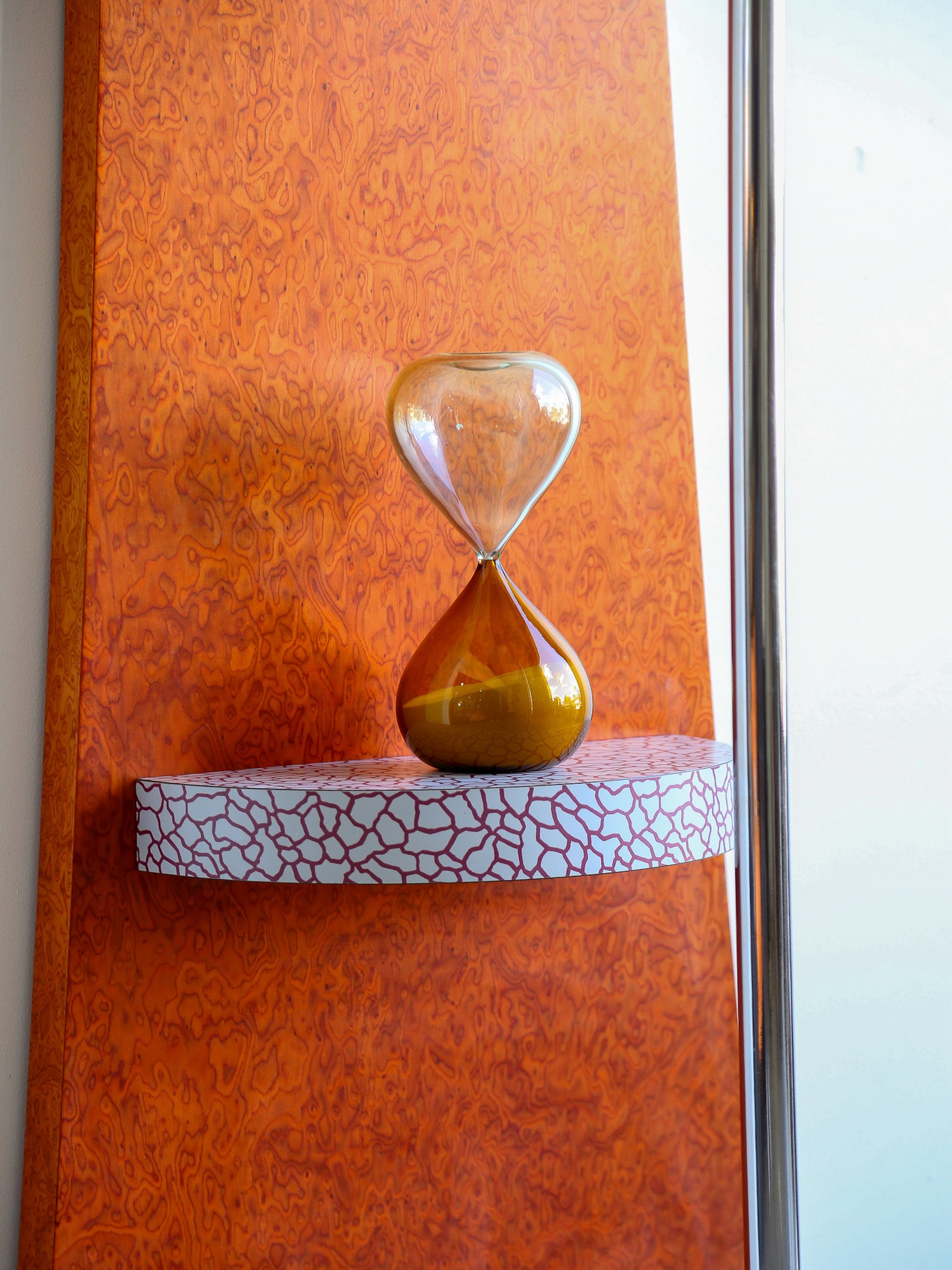Hourglass on a textured shelf against an orange wall
