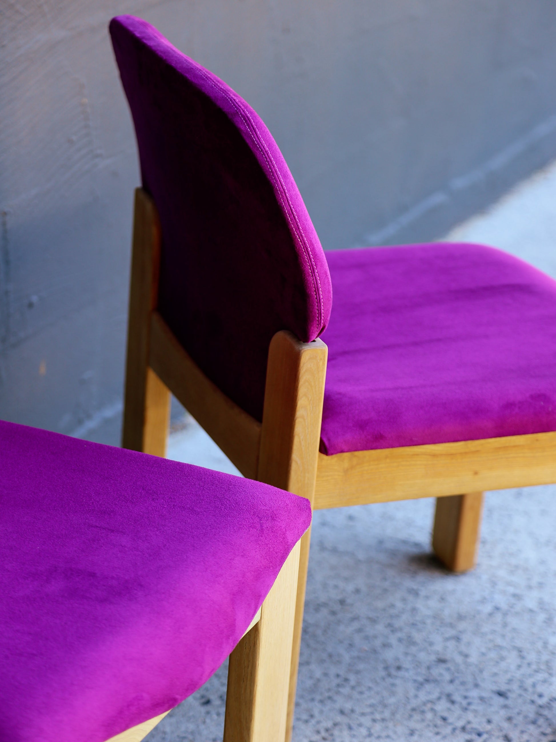 Two purple chairs with wooden frames on a gray floor.