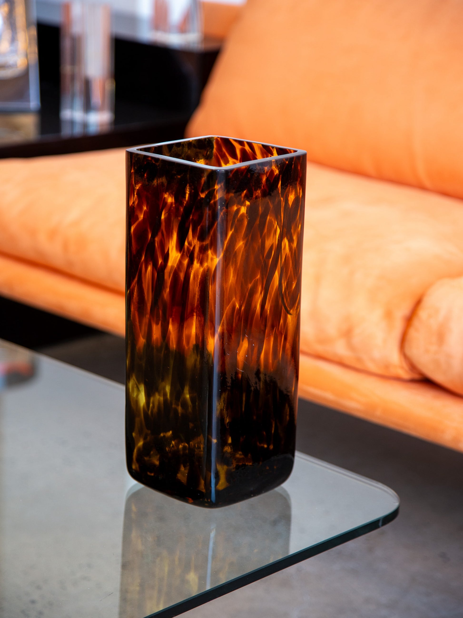 Italian vintage tortoiseshell glass vase in Murano style, displayed on a glass coffee table with an orange suede sofa in the background
