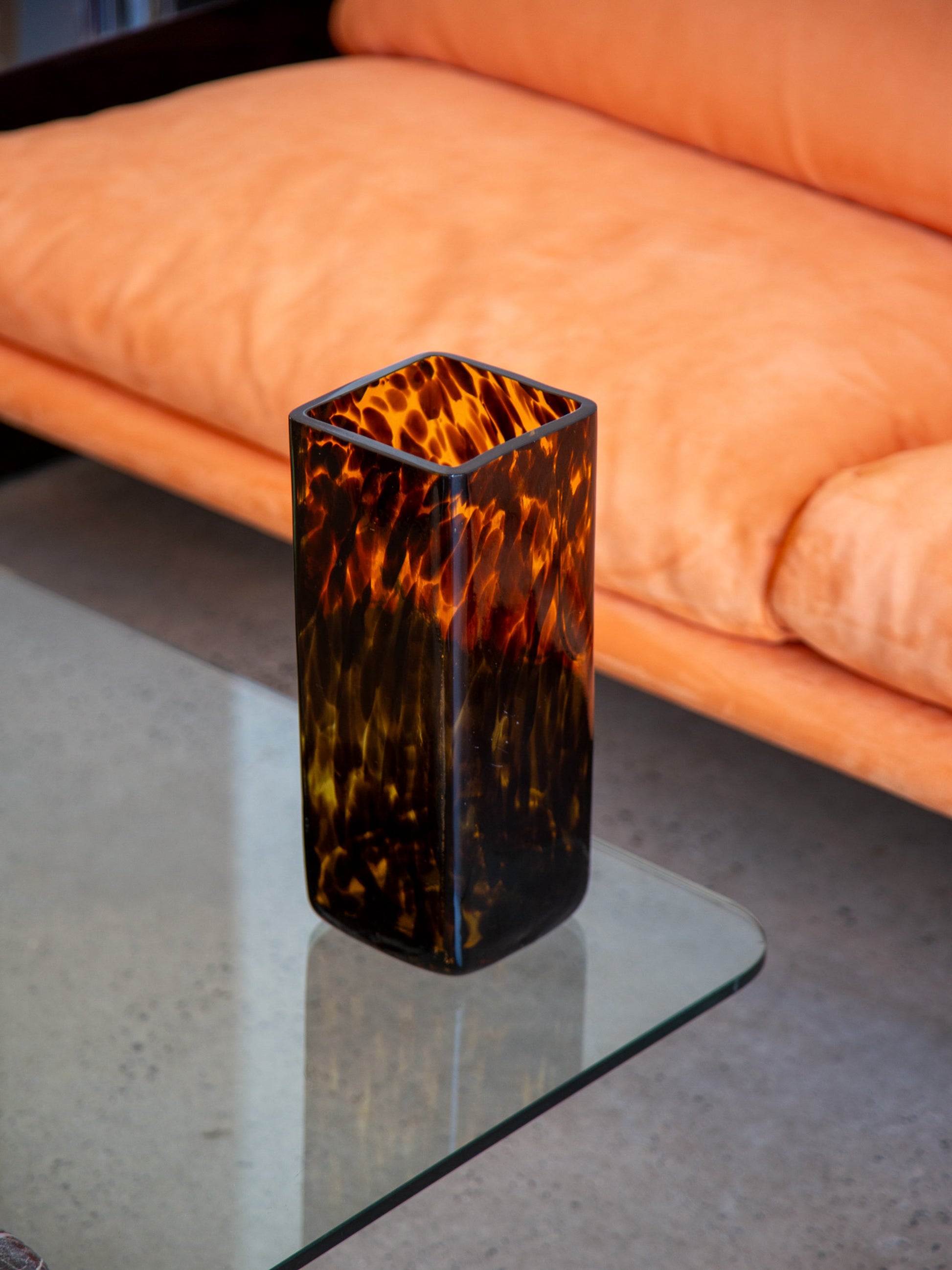Vintage Italian Murano glass vase with amber tortoiseshell effect, interior setting with soft orange upholstery and concrete flooring

