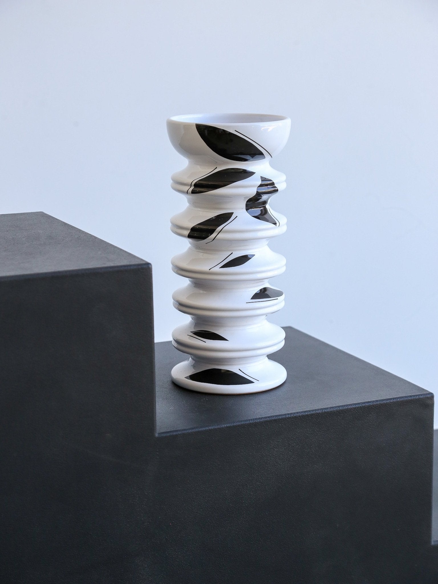 White vase with black spiral patterns on a dark surface and light gray background