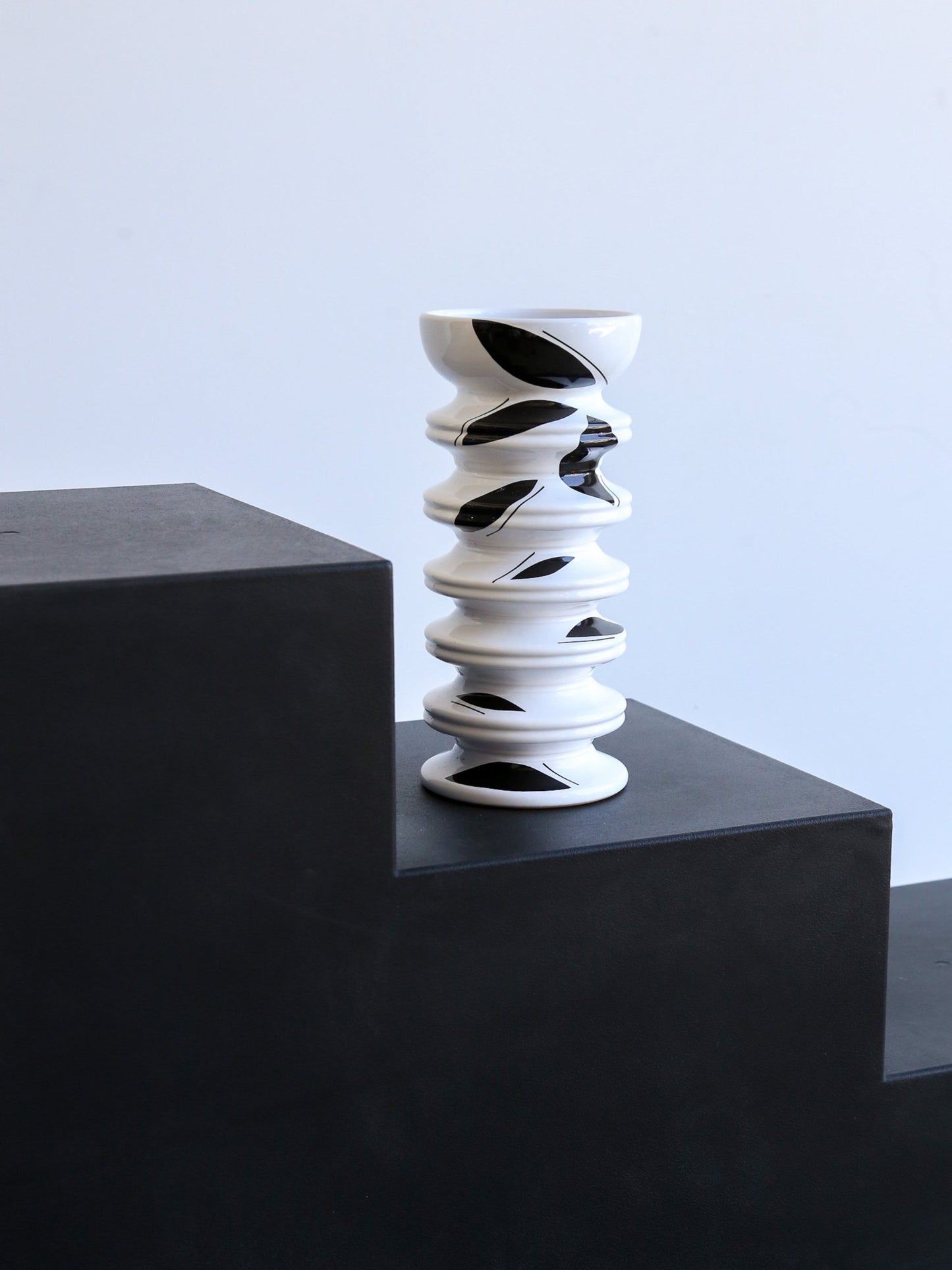 Black and white spiral vase on a dark surface with a light blue background