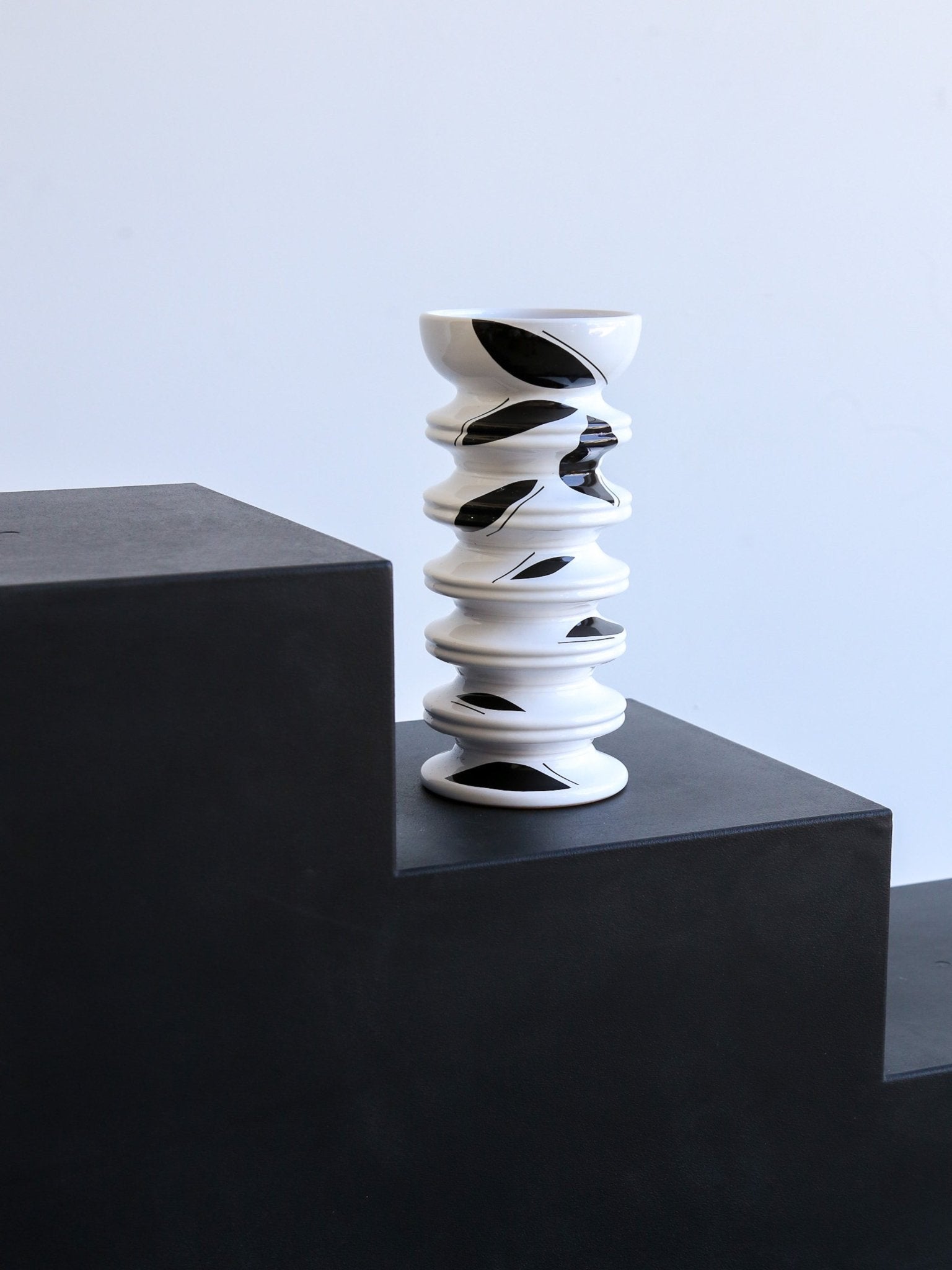 Black and white spiral vase on a dark surface with a light blue background