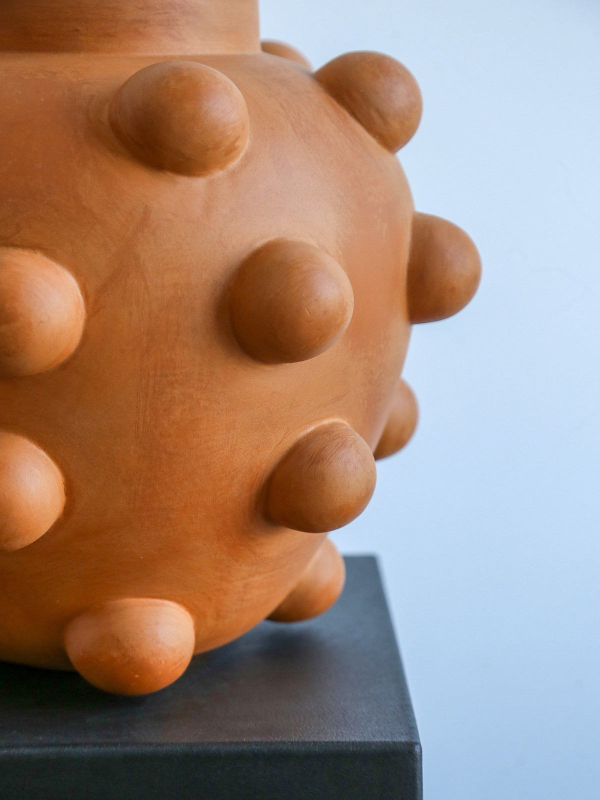 Terracotta vase with spherical protrusions on a light blue background