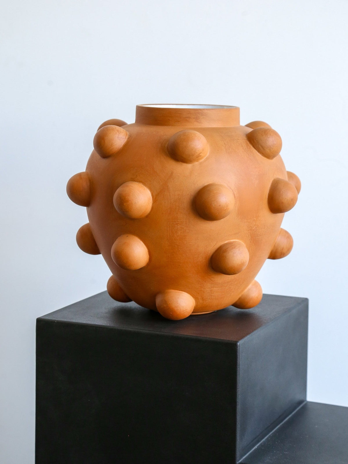 Ceramic vase with textured surface on a black pedestal against a light blue background