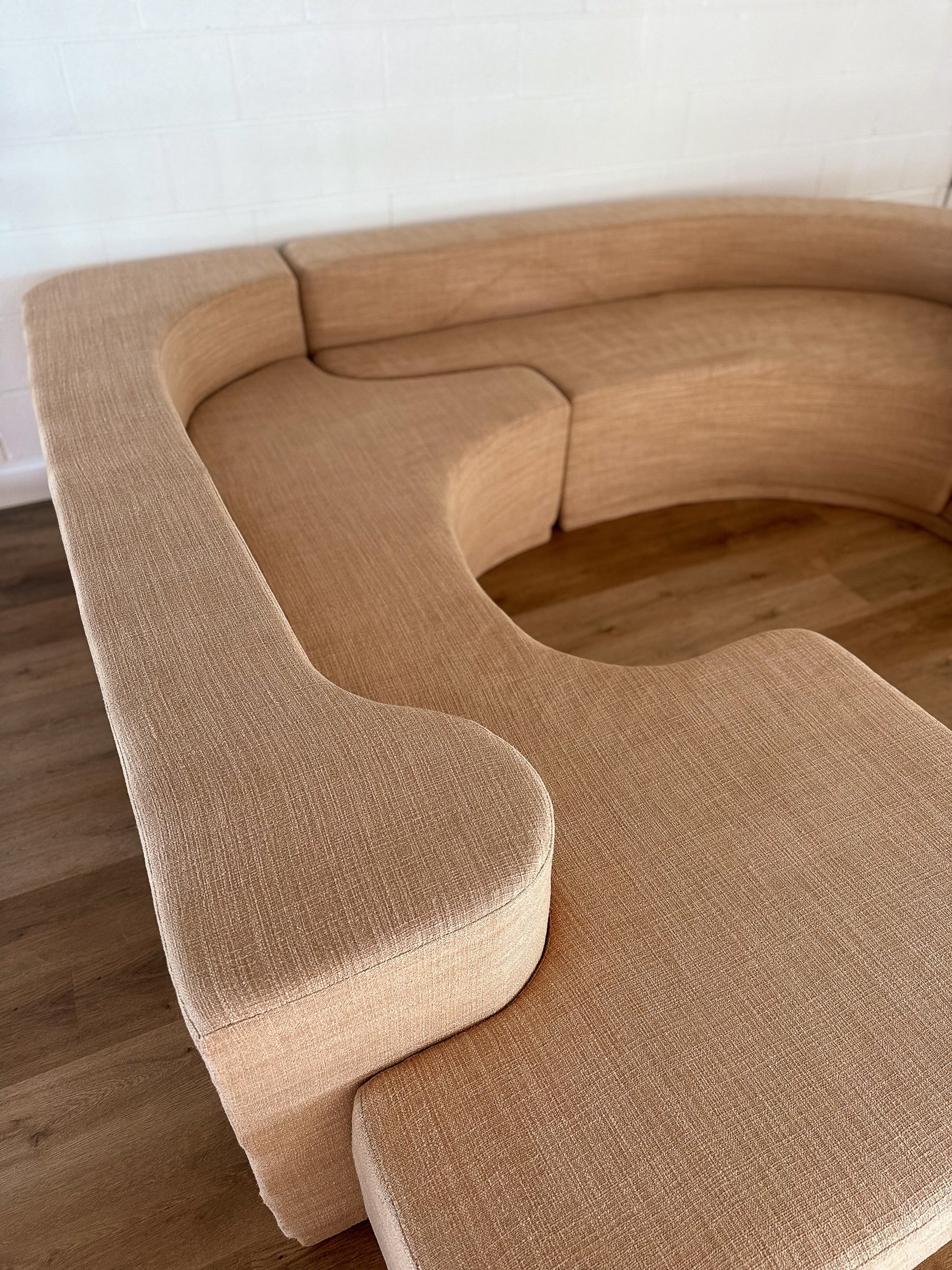 Beige curved sofa in a minimalistic room with wooden floor.