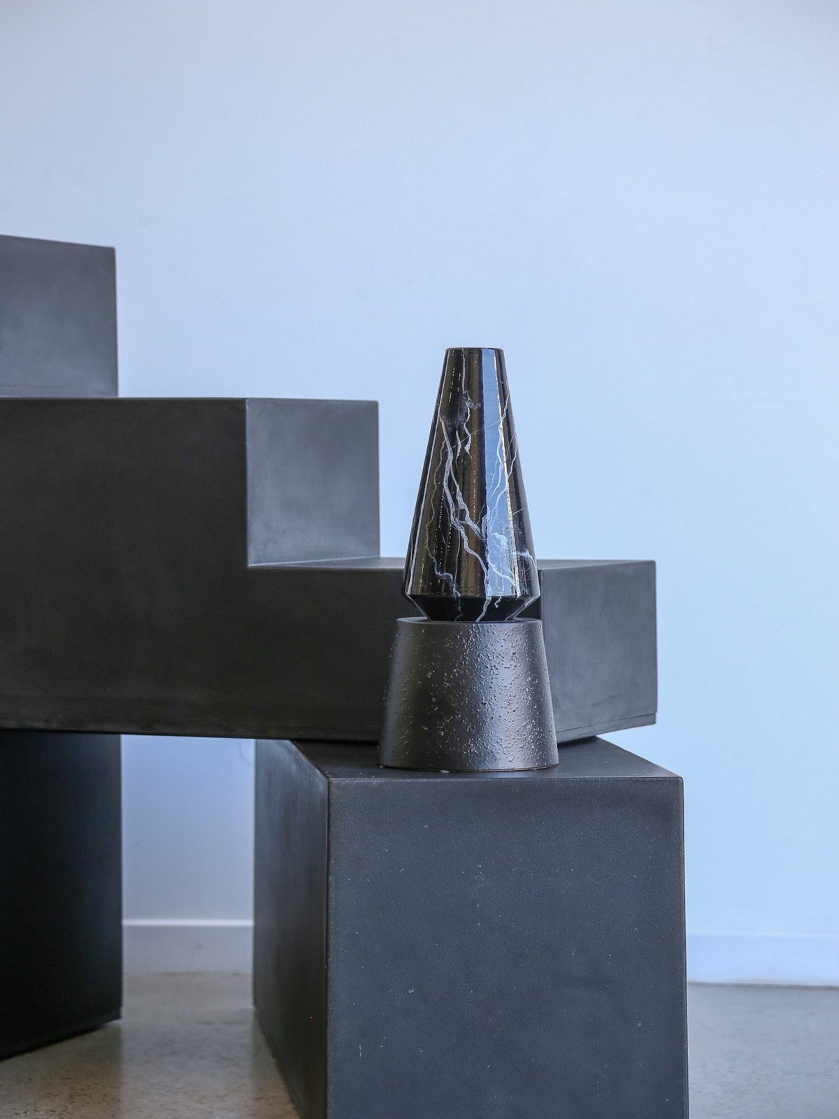 Abstract sculpture with geometric shapes and a marble-textured cone on a light blue background