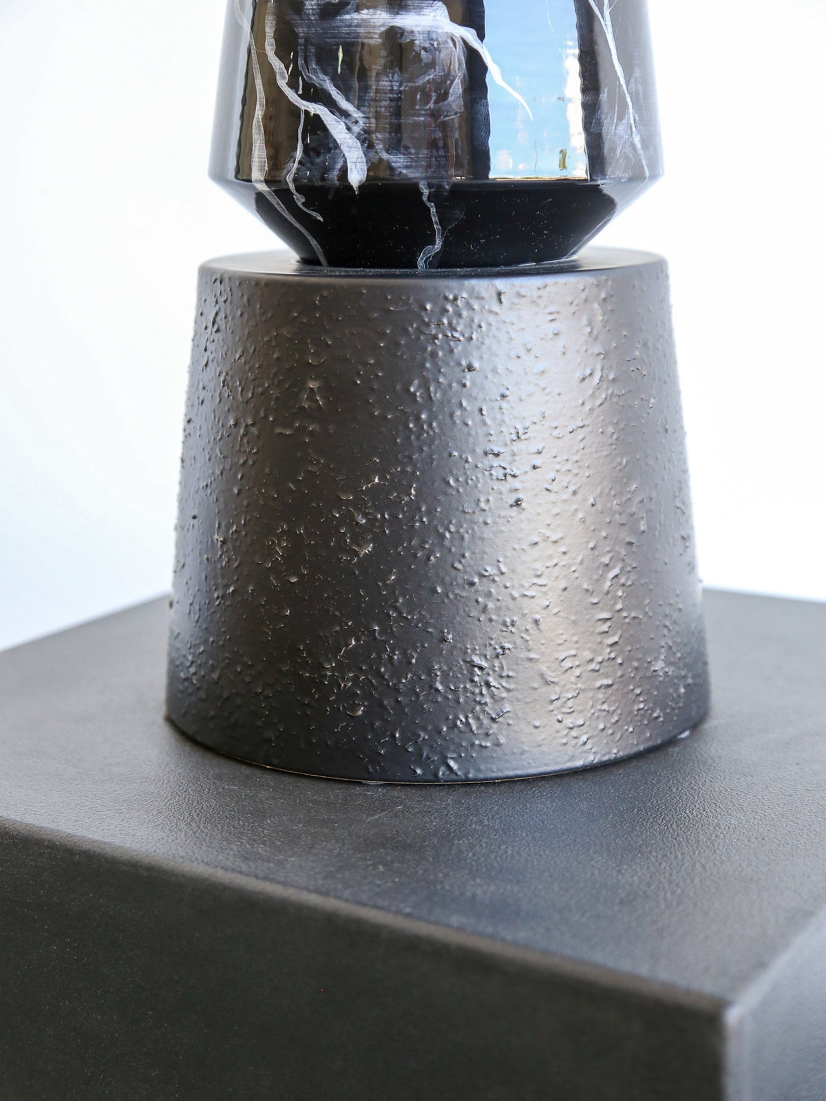 Black and white marbled vase on a textured gray pedestal against a light background