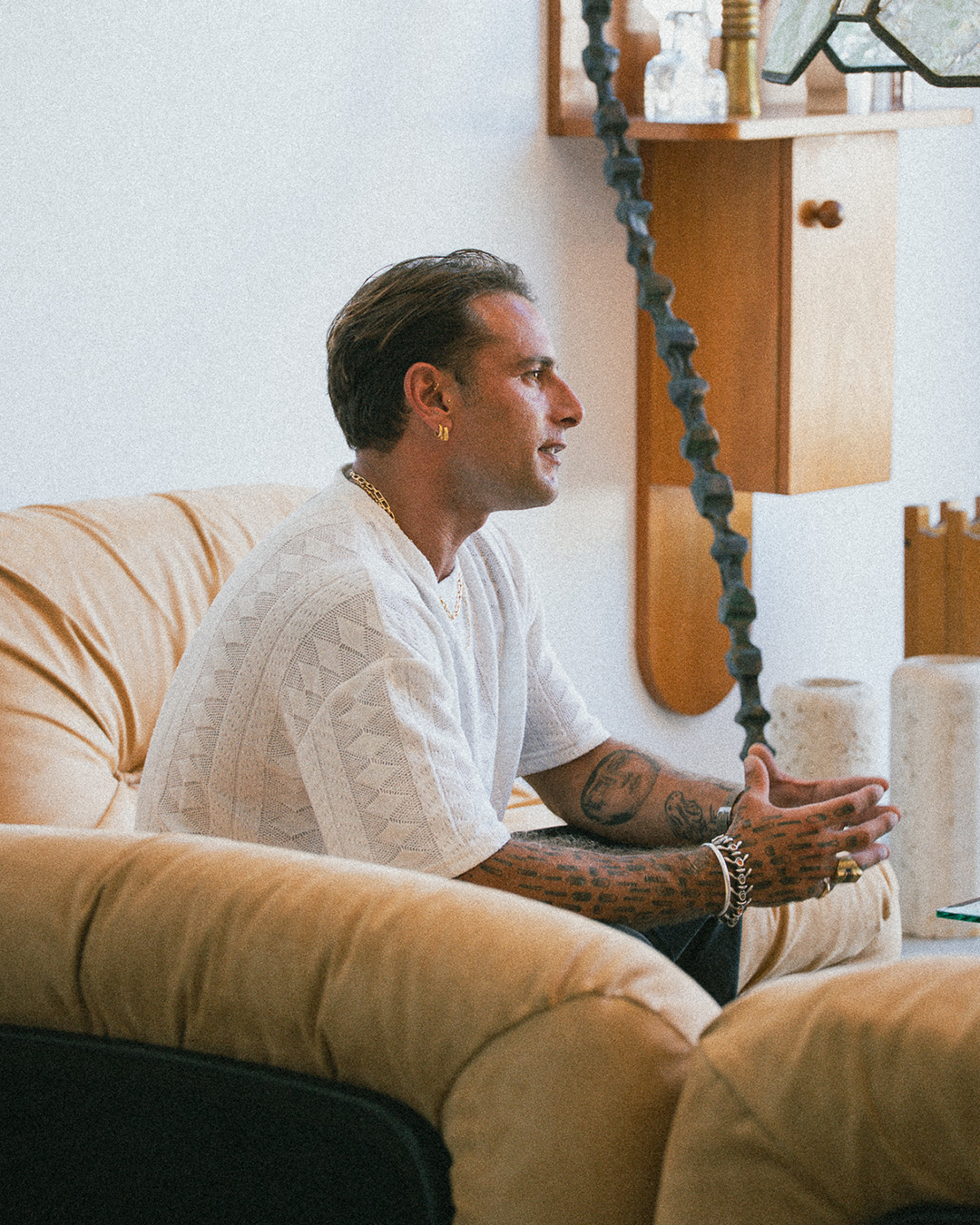 Man sitting on a beige couch in a room with wooden shelves and decorative items.