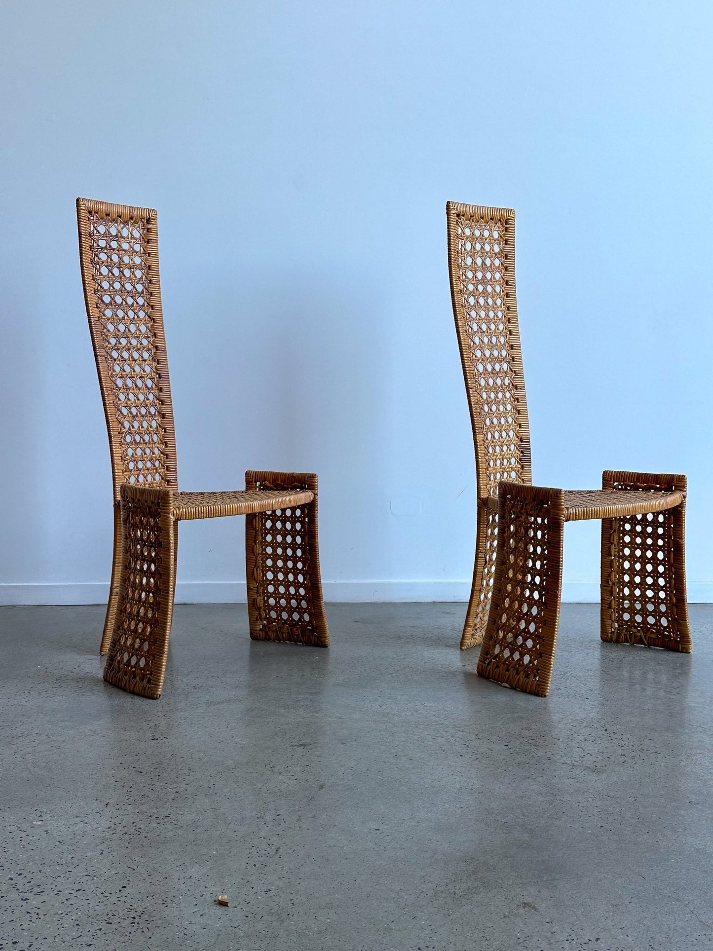 Two wicker chairs on a concrete floor with a light blue wall background