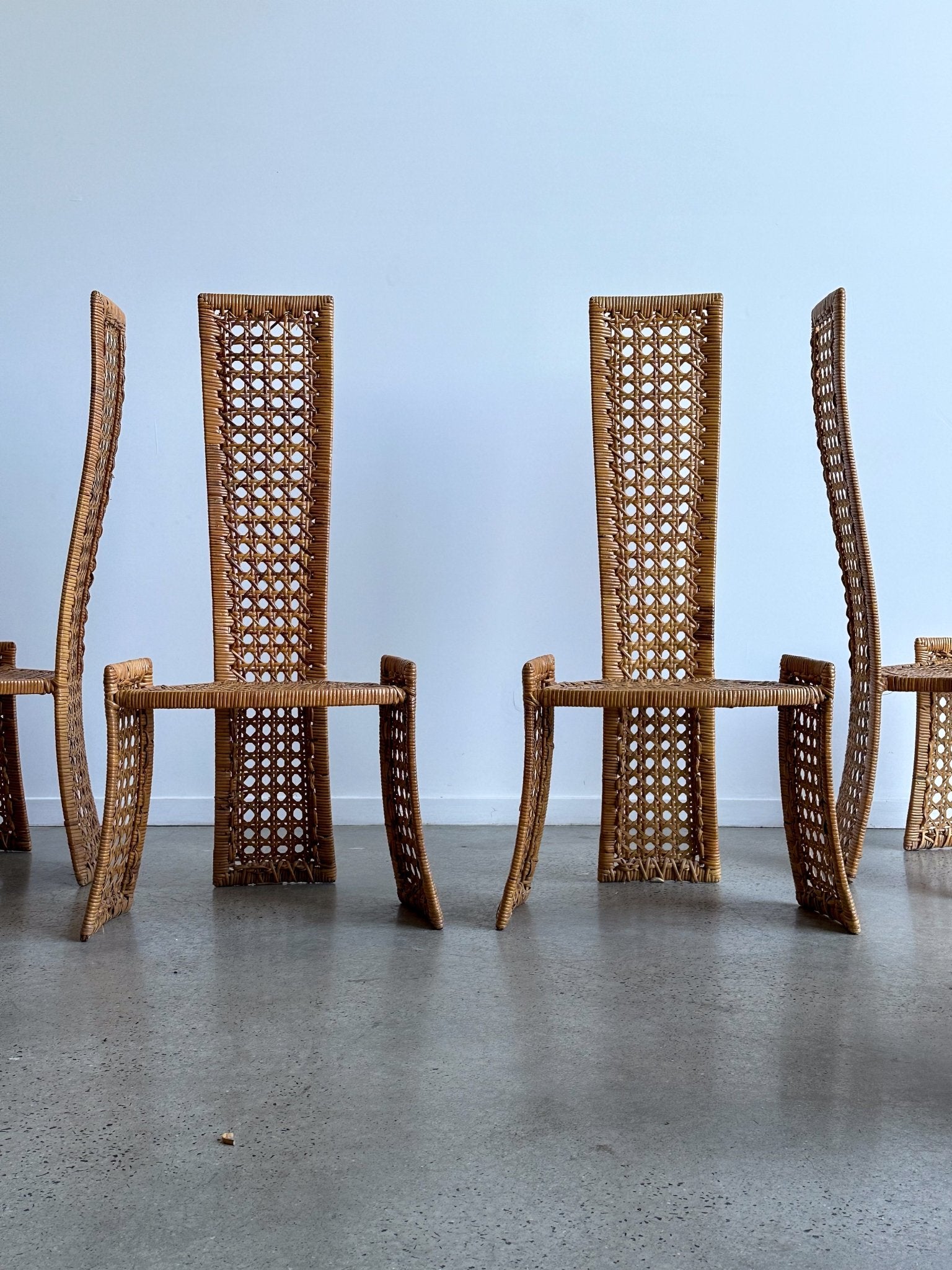 Woven wooden chairs on a concrete floor with a light blue wall background