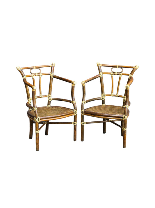 Two matching bamboo armchairs with woven cane seats and brass hardware, shown side by side on a plain white background.