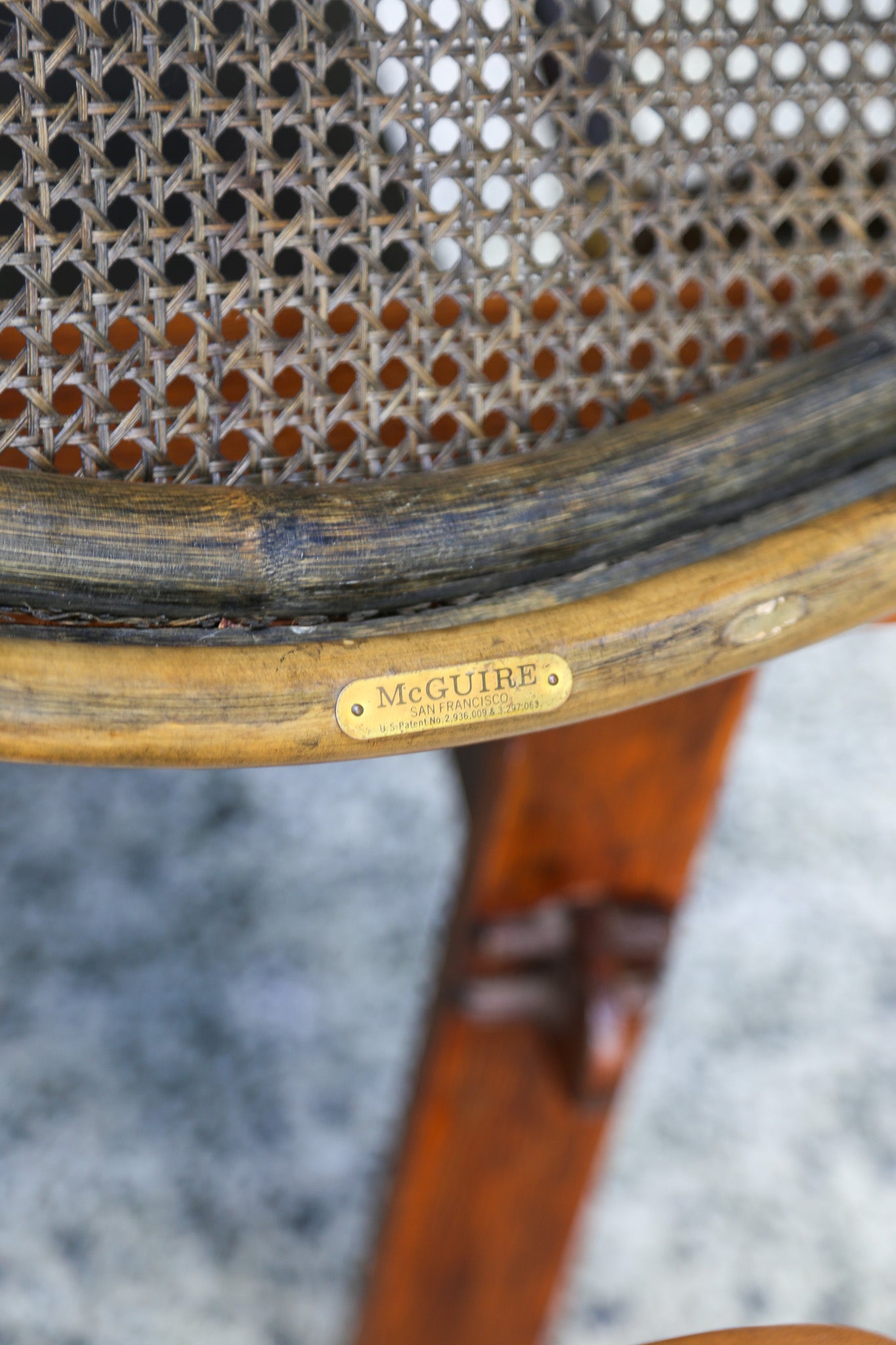 Close-up of a vintage cane and wood chair back, showing a brass McGuire brand plate on the wooden frame.