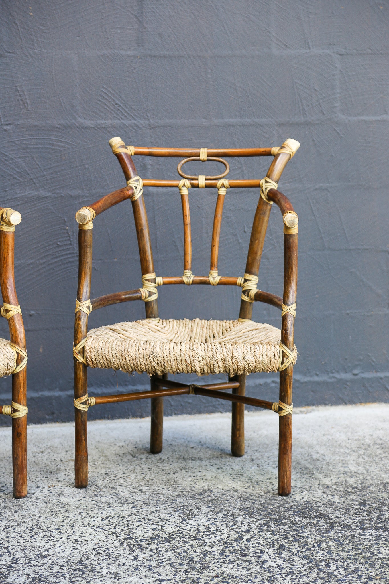 A rustic wooden dining chair with a woven straw seat and light-colored metal accents, positioned against a dark gray textured wall.
