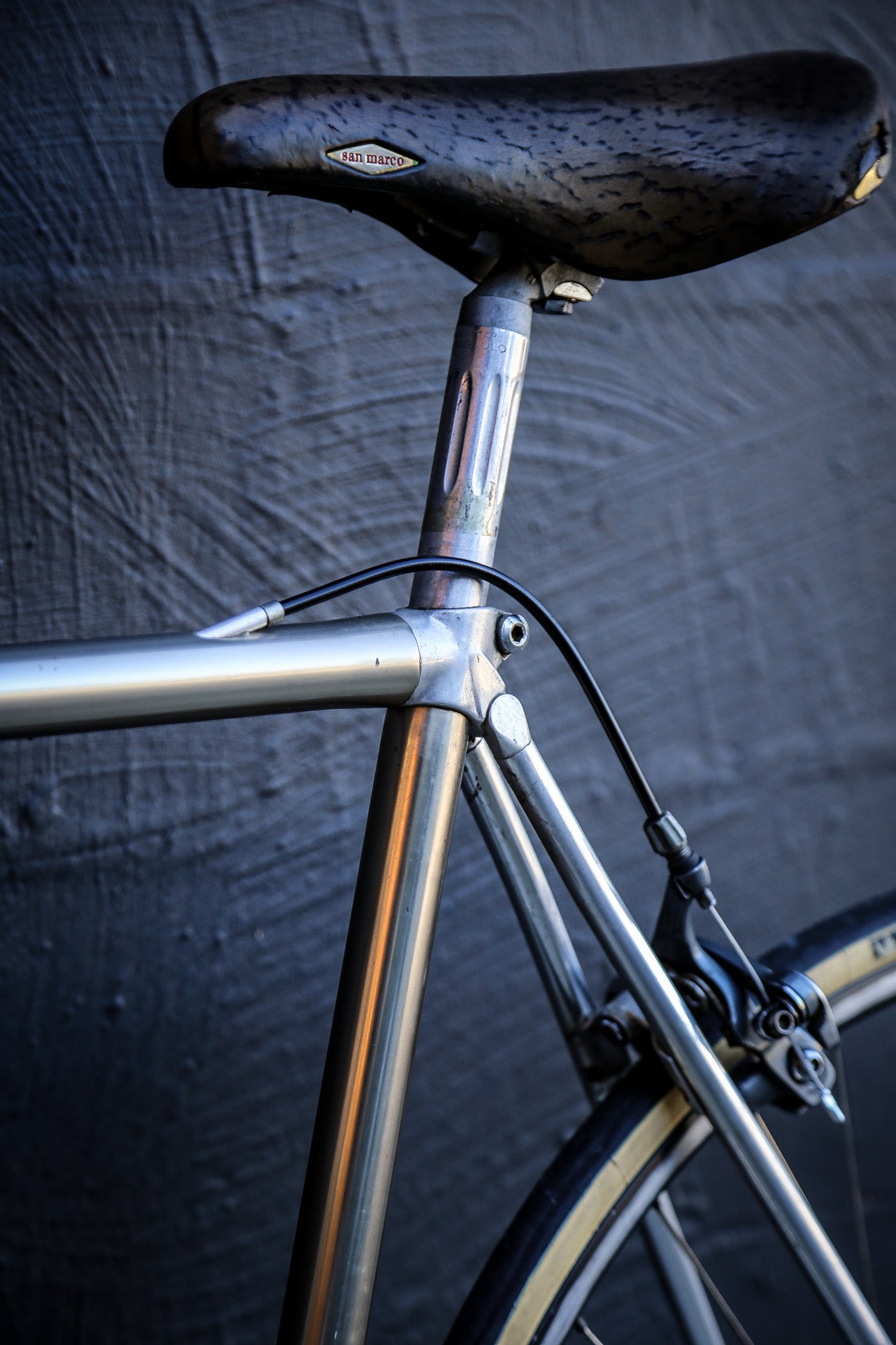 Close-up of a vintage bicycle frame with a black saddle and silver metal tubing, set against a dark textured background.