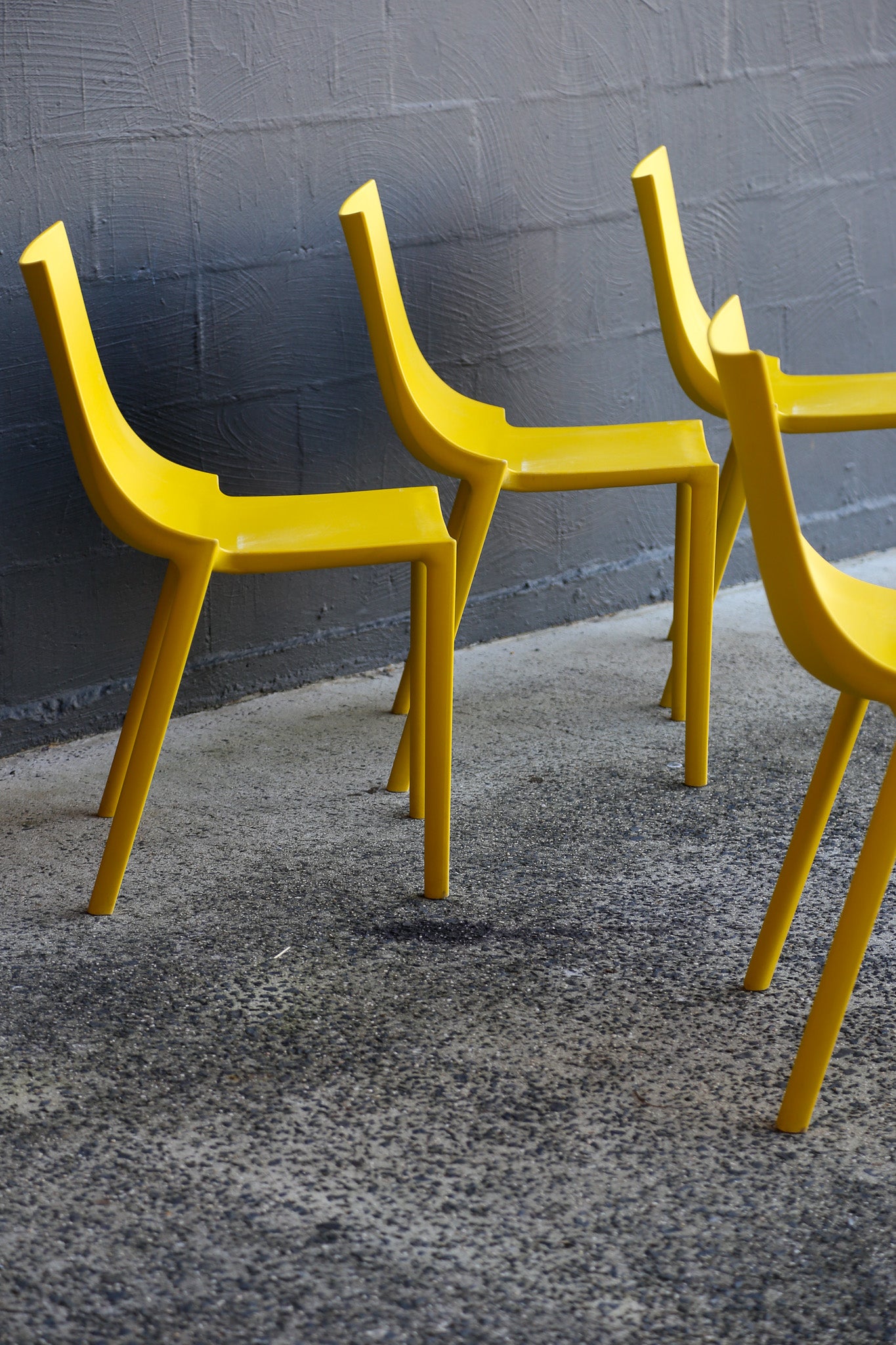 Four yellow chairs against a gray wall on a textured gray floor.