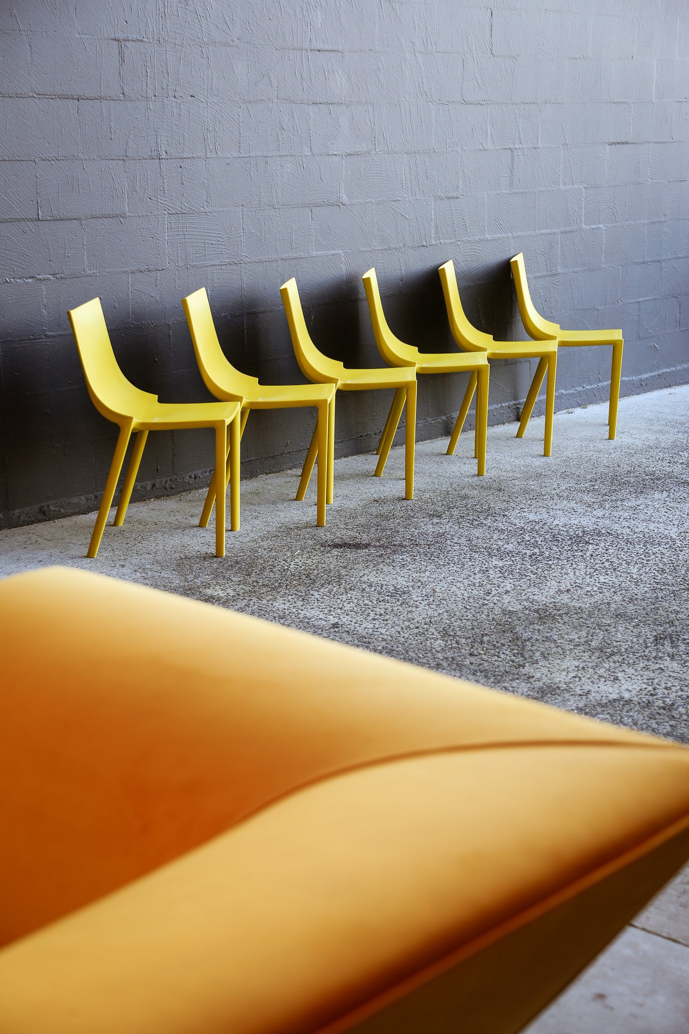 Yellow chairs lined up against a gray wall with a blurred orange chair in the foreground.