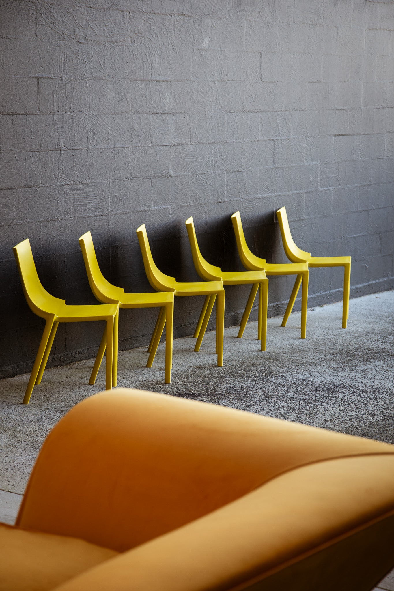 Yellow chairs lined up against a gray brick wall.