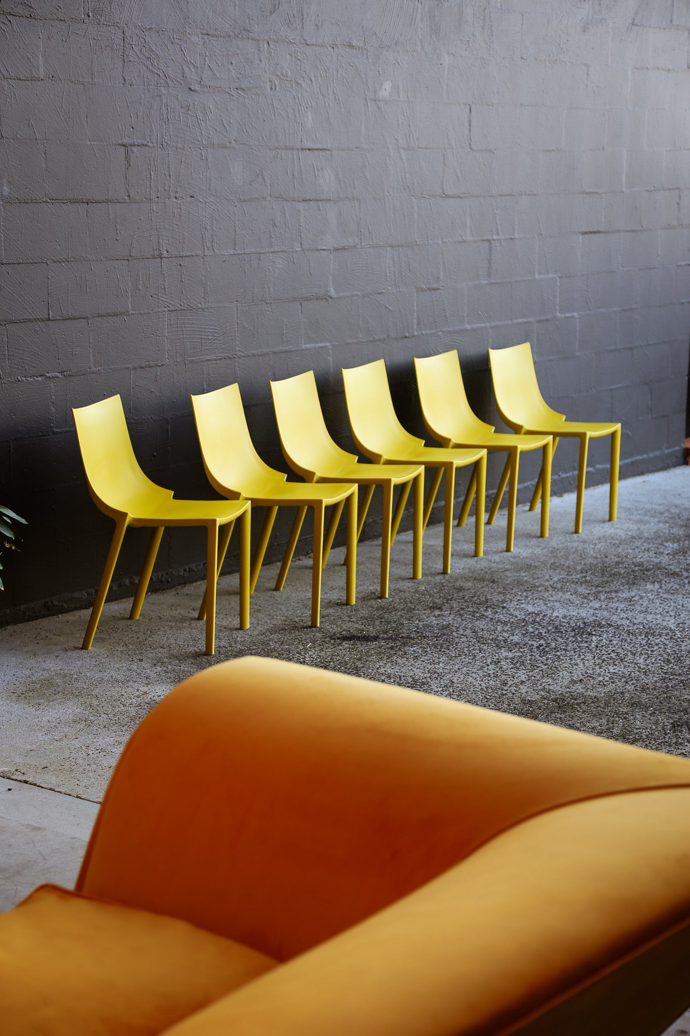 Yellow chairs lined up against a gray wall with an orange chair in the foreground.