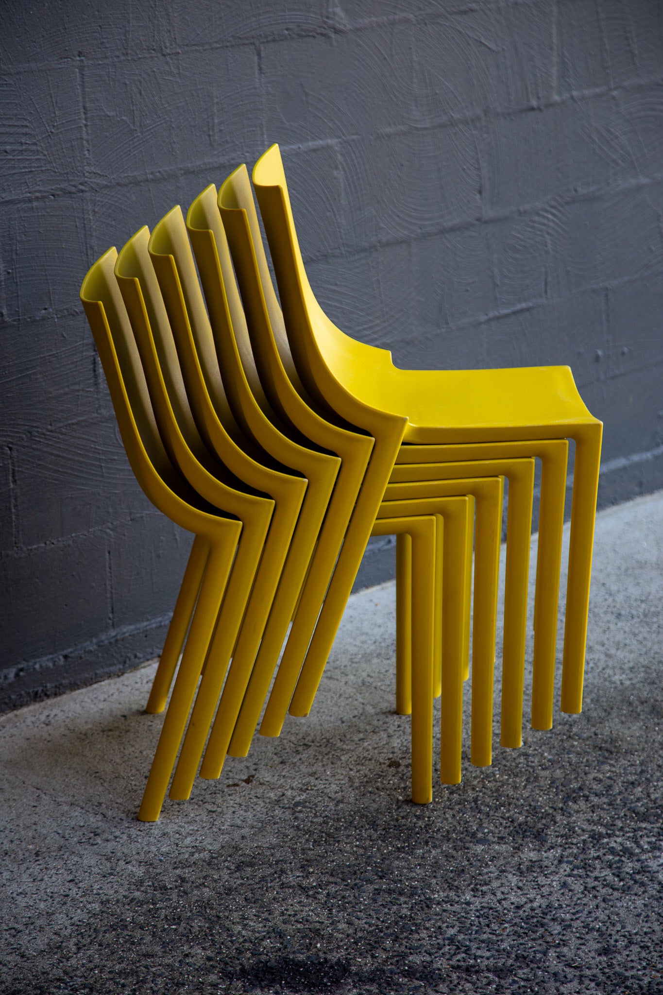Stack of yellow chairs against a gray textured wall.