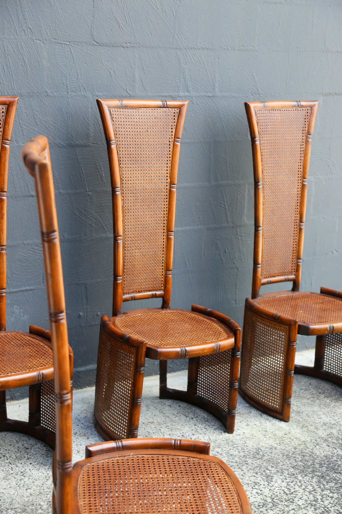 A set of mid-century modern bamboo and cane chairs arranged against a gray painted brick wall.