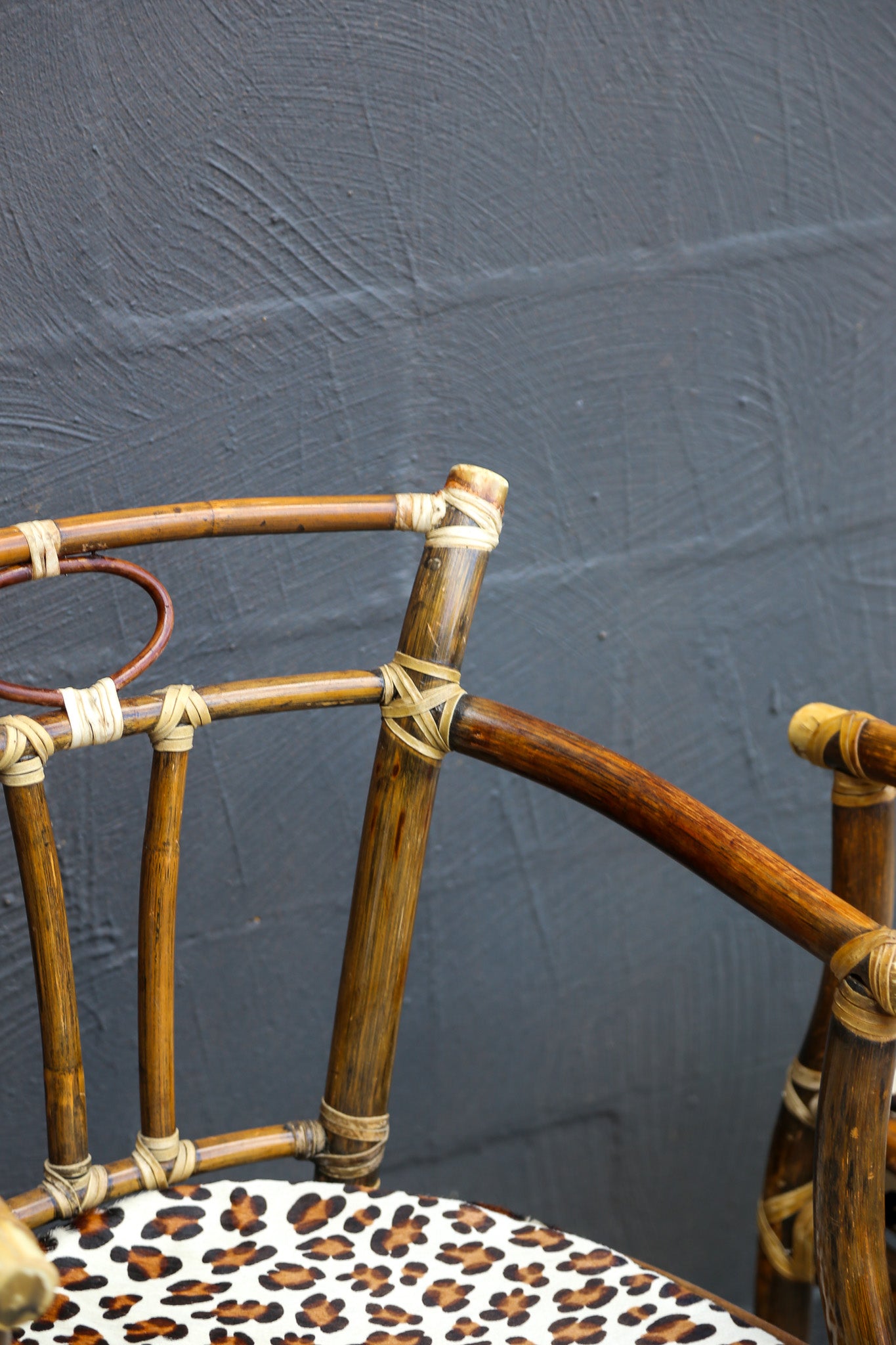 Close-up of a rustic bamboo chair with a leopard-print cushioned seat, set against a dark textured gray wall.