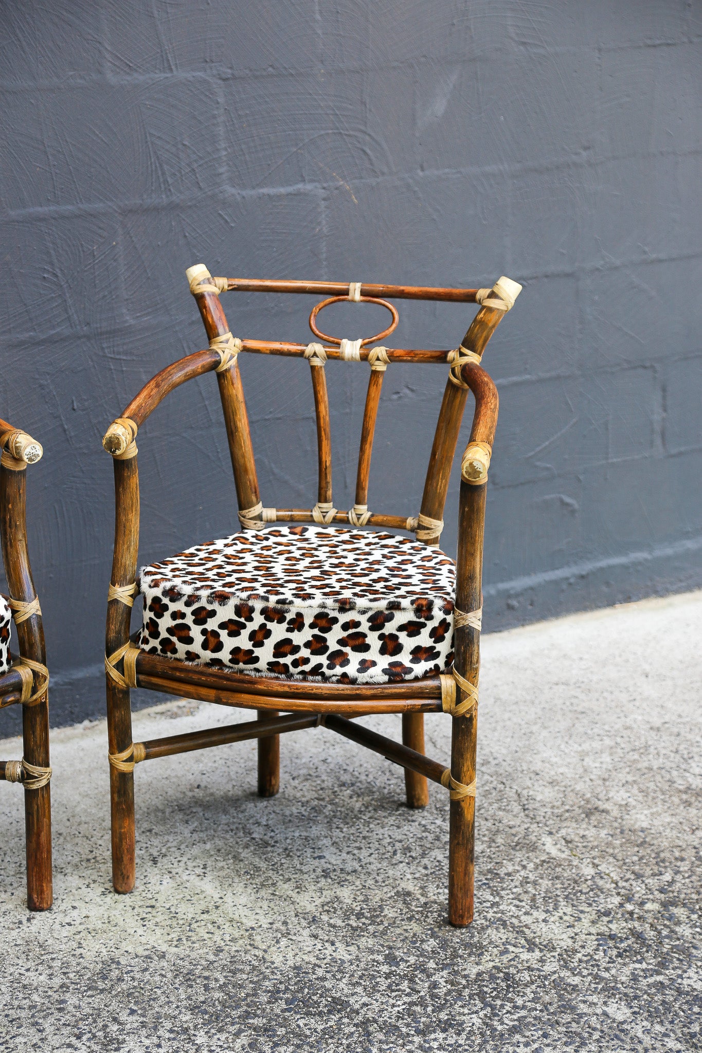 A rustic bamboo armchair with a leopard-print cushion, set against a dark gray brick wall.