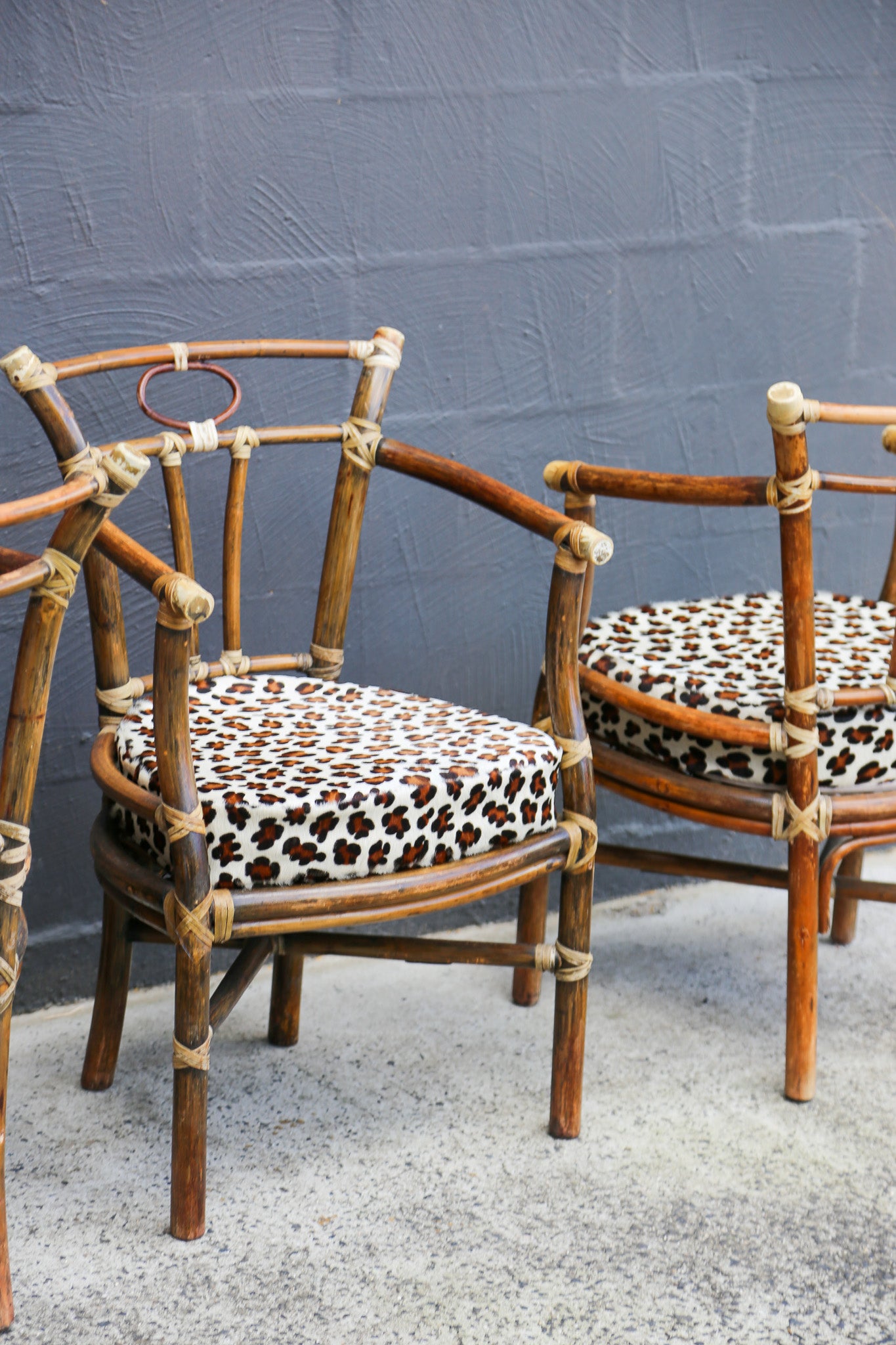 Two rattan armchairs with leopard-print seat cushions, positioned against a gray painted brick wall.