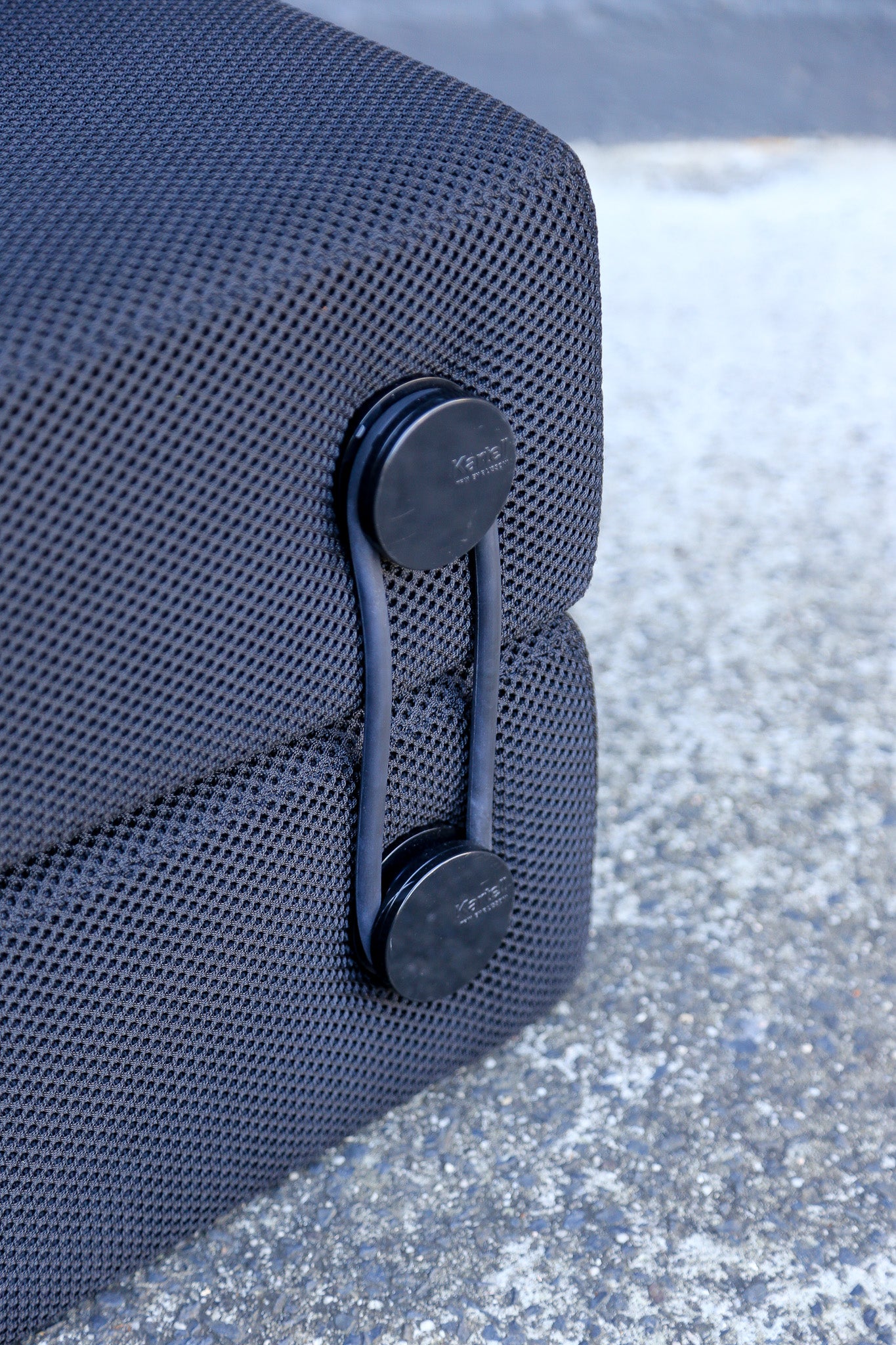 Close-up of a dark gray textured mesh outdoor furniture cushion secured with two black quick-release straps on a concrete surface.
