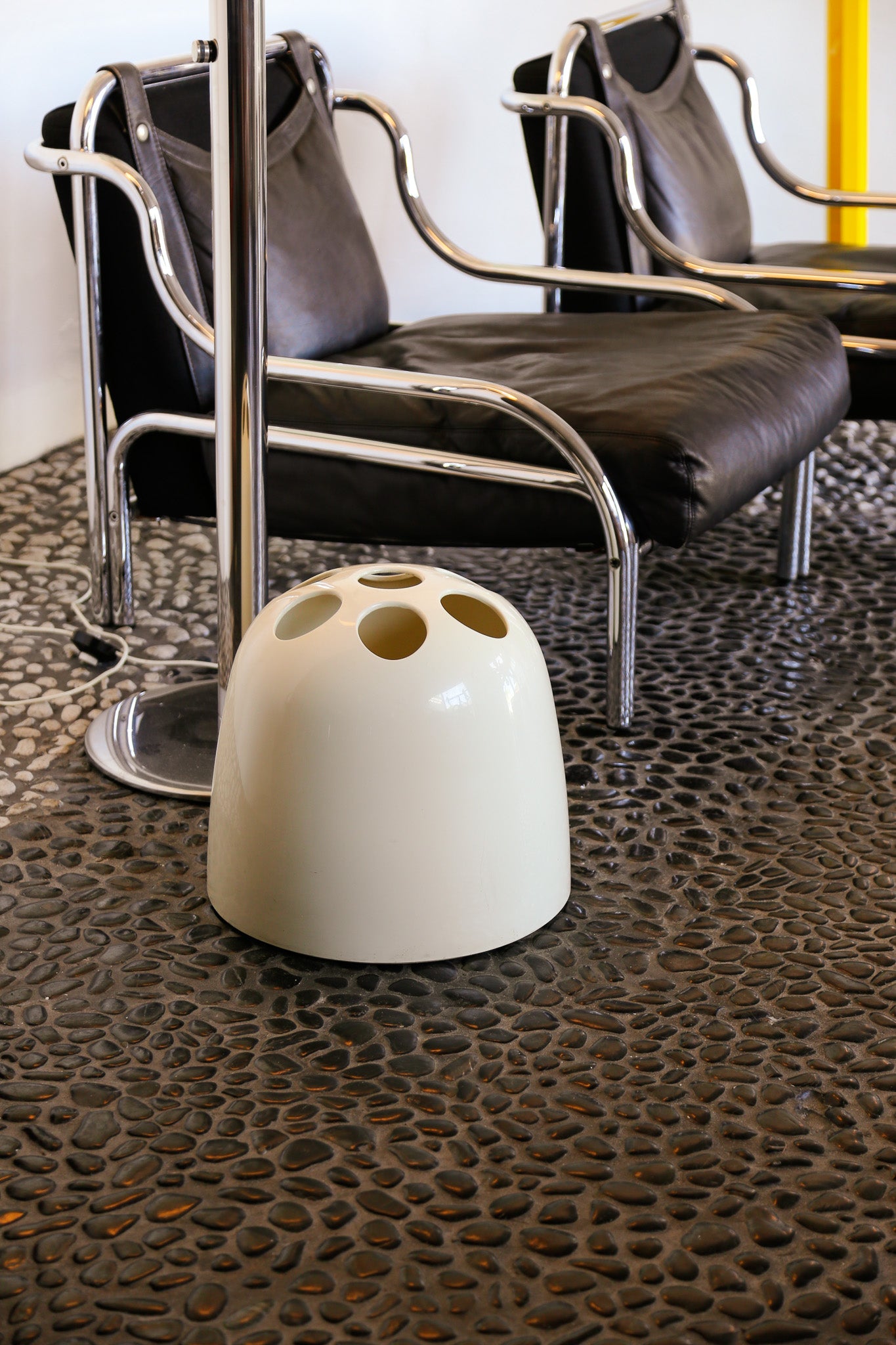 White ceramic object on a textured floor with modern chairs in the background