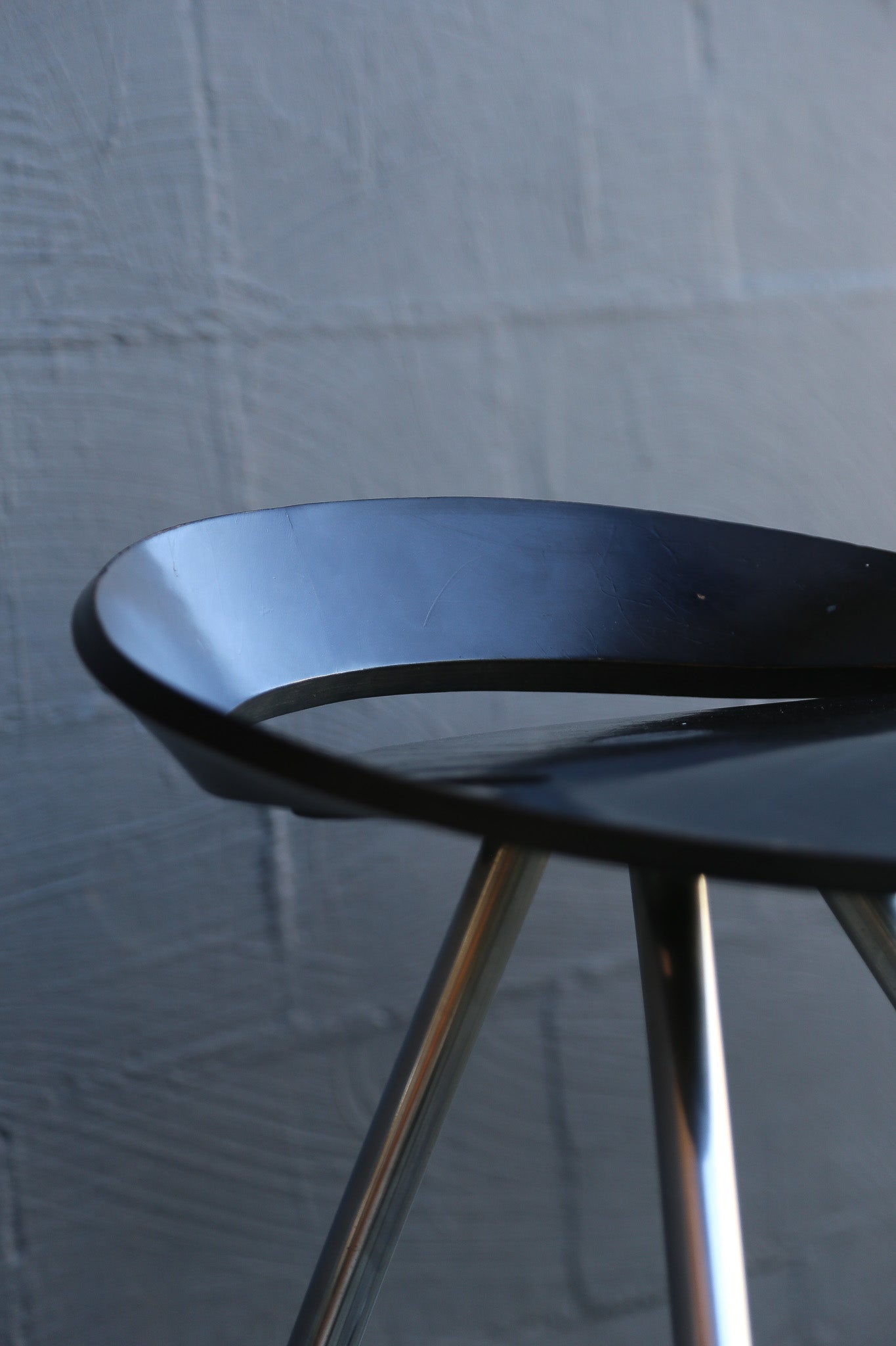 Black stool with metal legs against a textured gray wall
