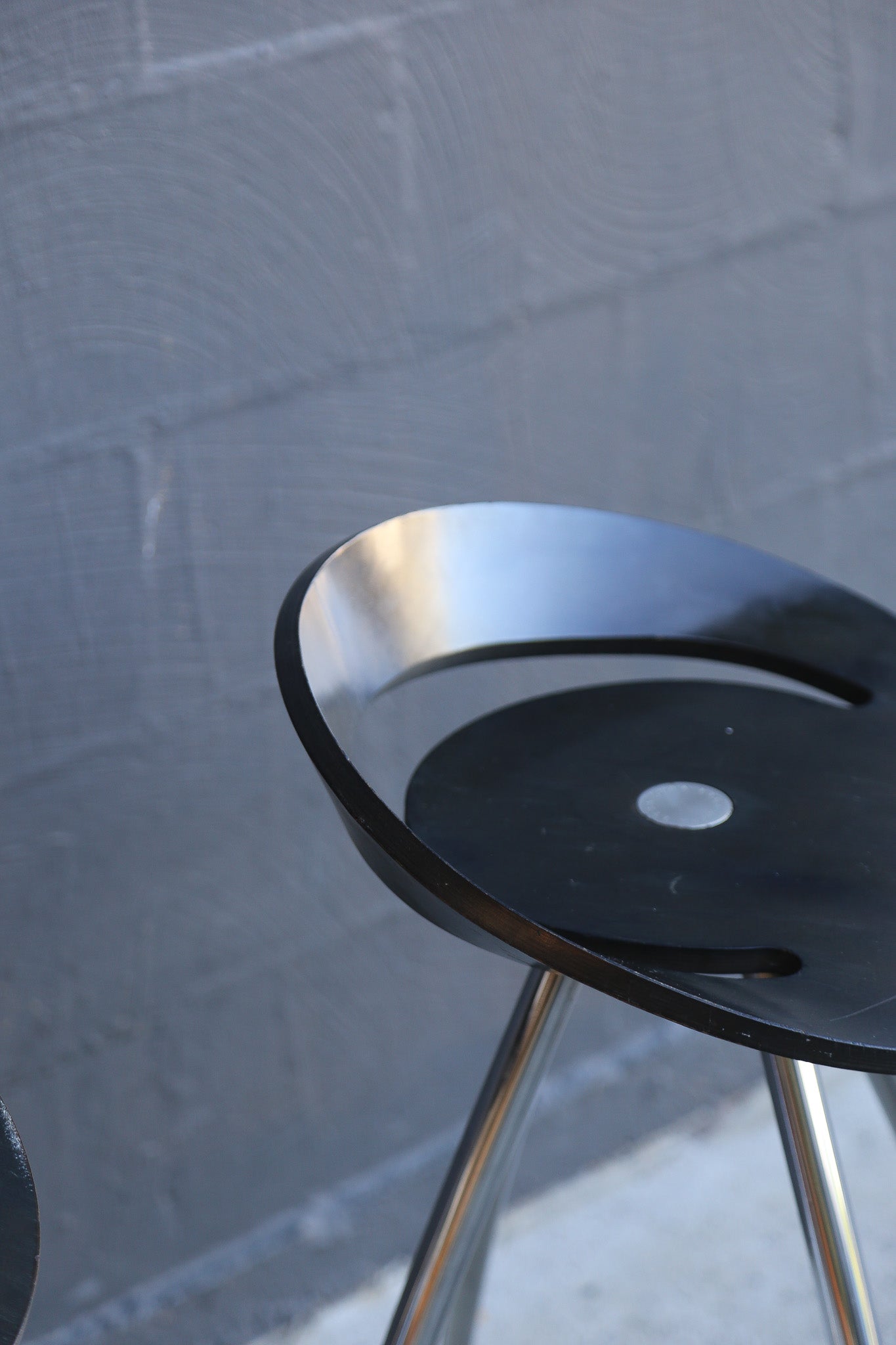 Black stool with metal legs against a textured gray wall